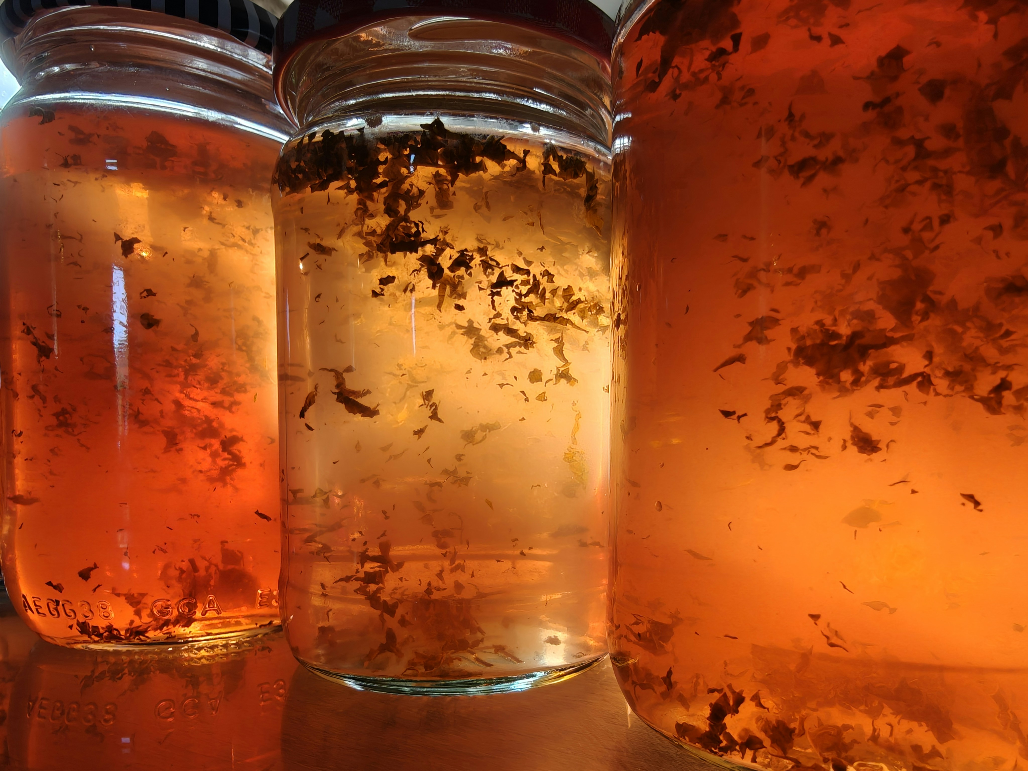 Jars of apple jelly, golden in colour, lit by sunlight from behind. The jelly is flecked with mint.