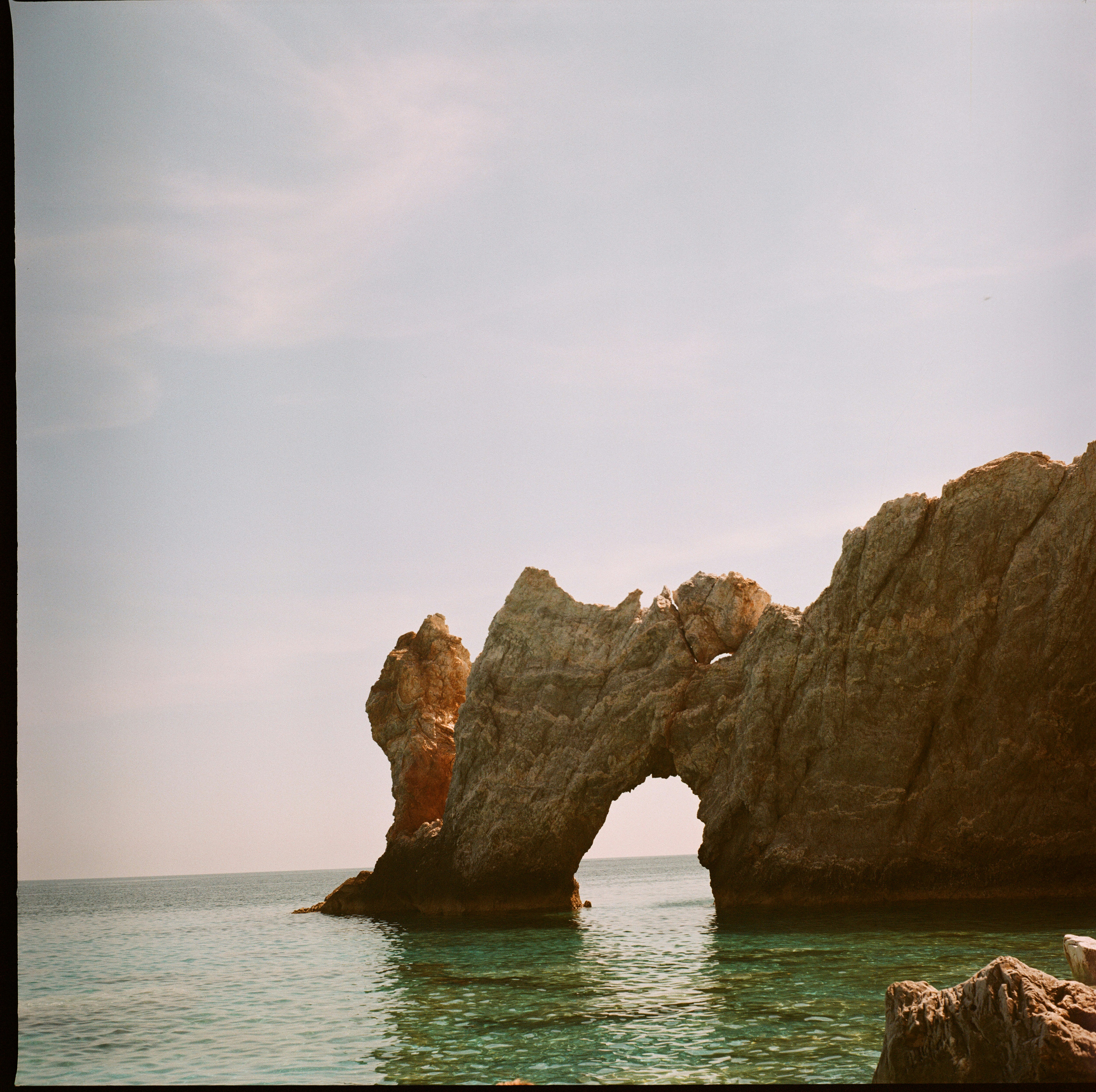 A natural stone arch rising from clear turquoise water under a pale sky