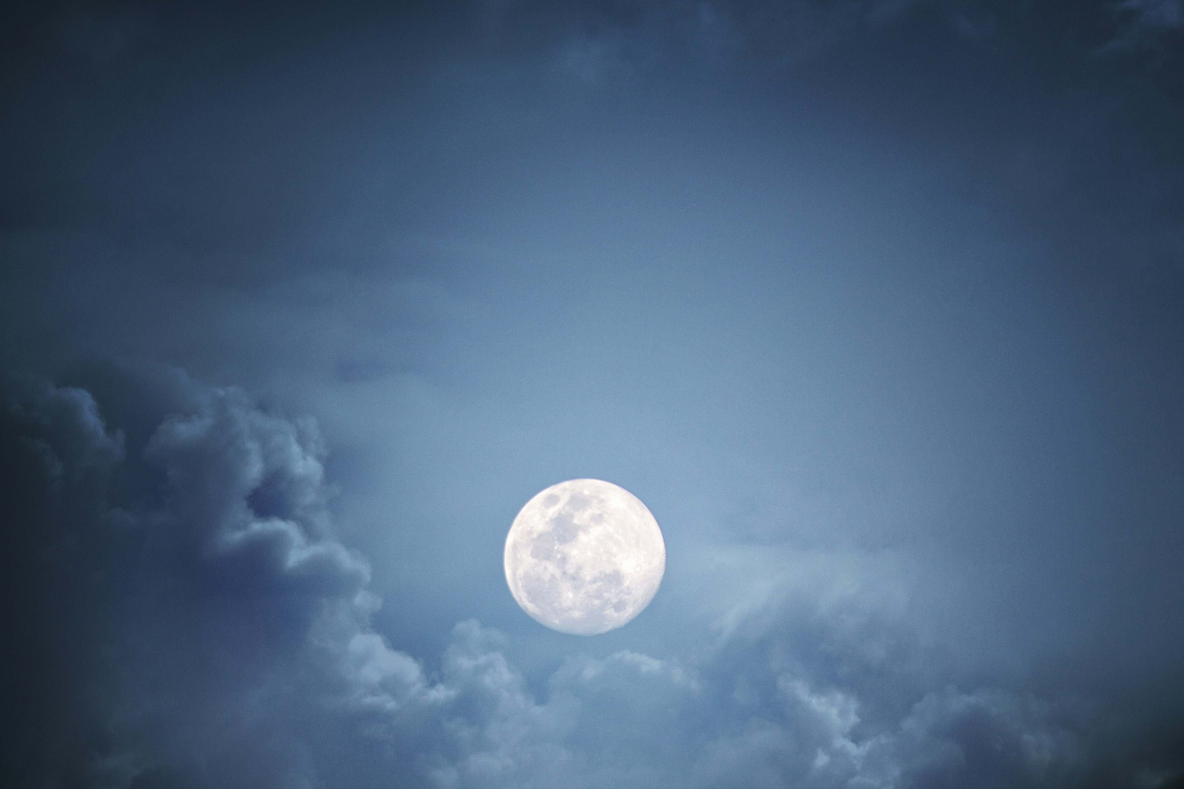 A full moon glowing in a dark blue sky surrounded by soft clouds