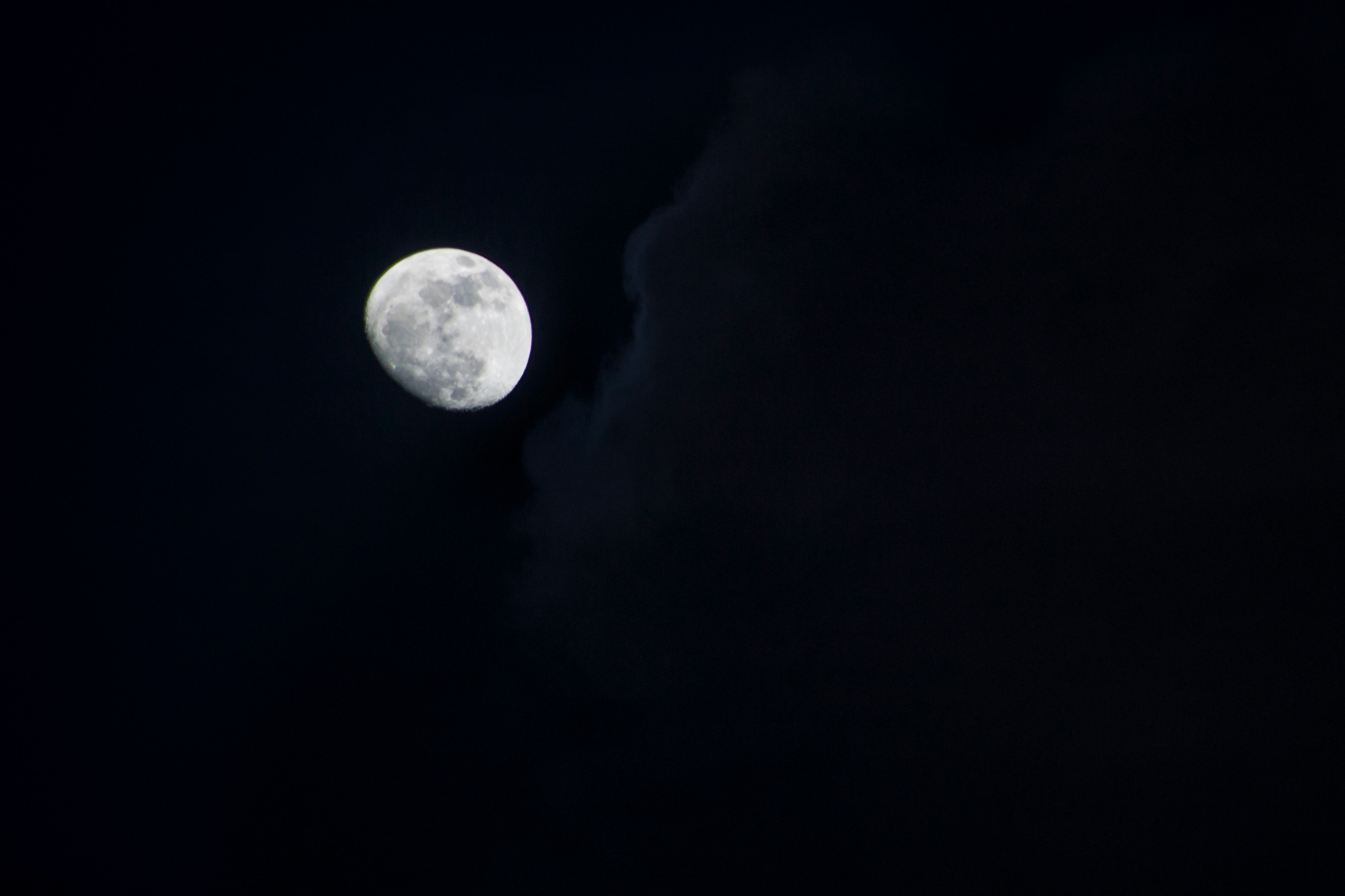 A bright moon in a dark night sky partially obscured by a cloud