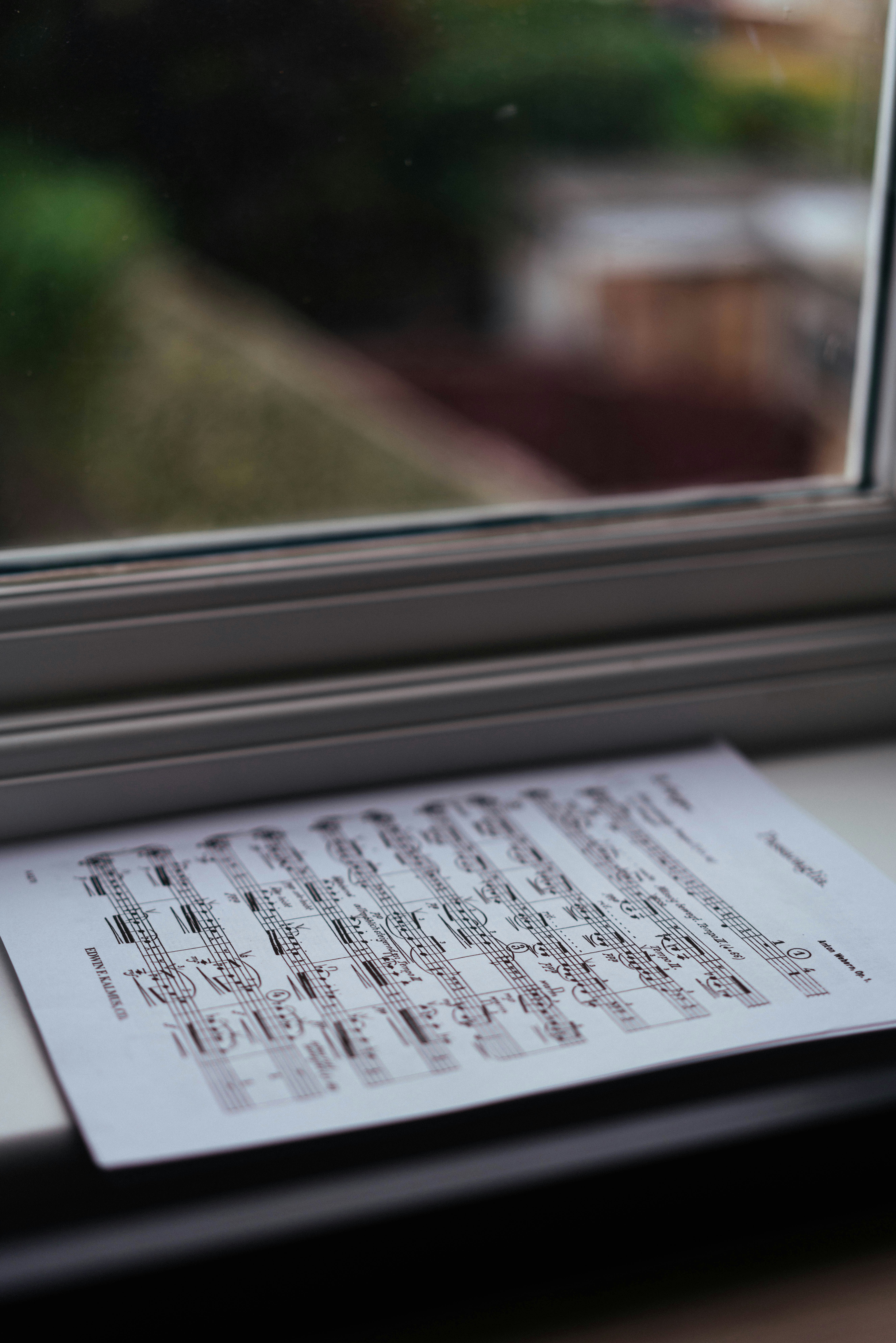 Sheet music resting on a white windowsill with a blurred outdoor view