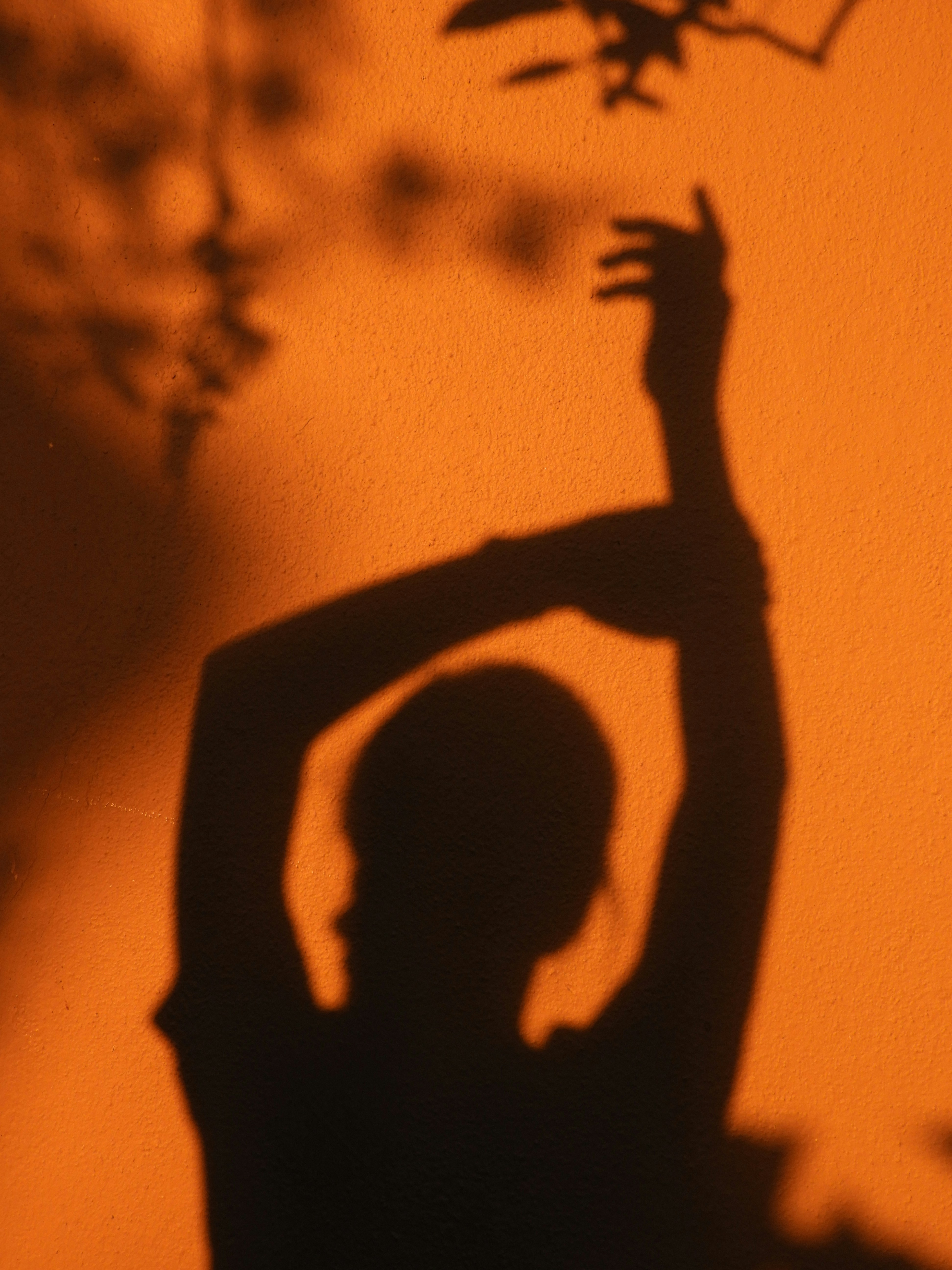 A silhouette of a person with arms raised against a warm orange wall