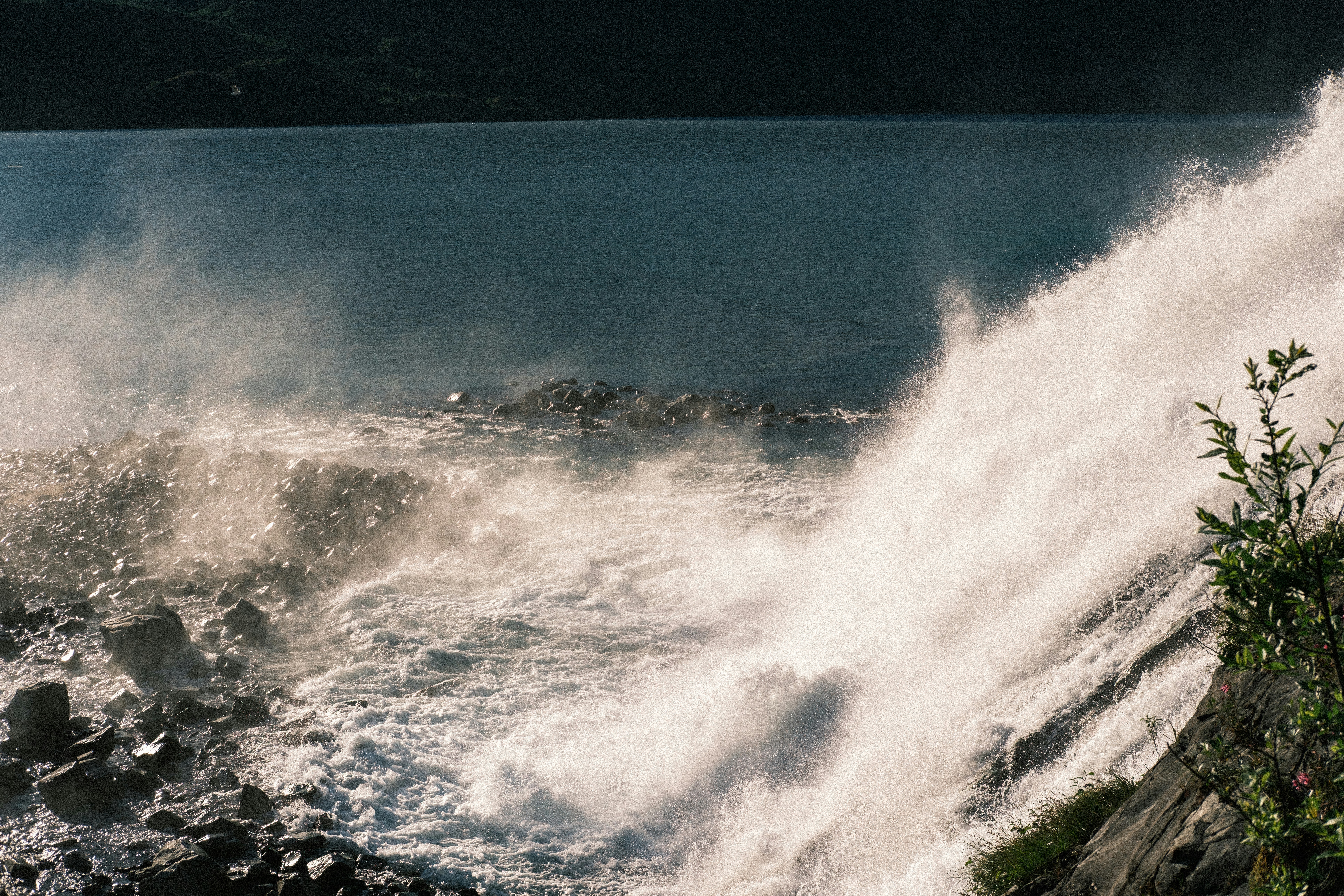 A powerful waterfall cascading over dark rocks into a deep blue lake