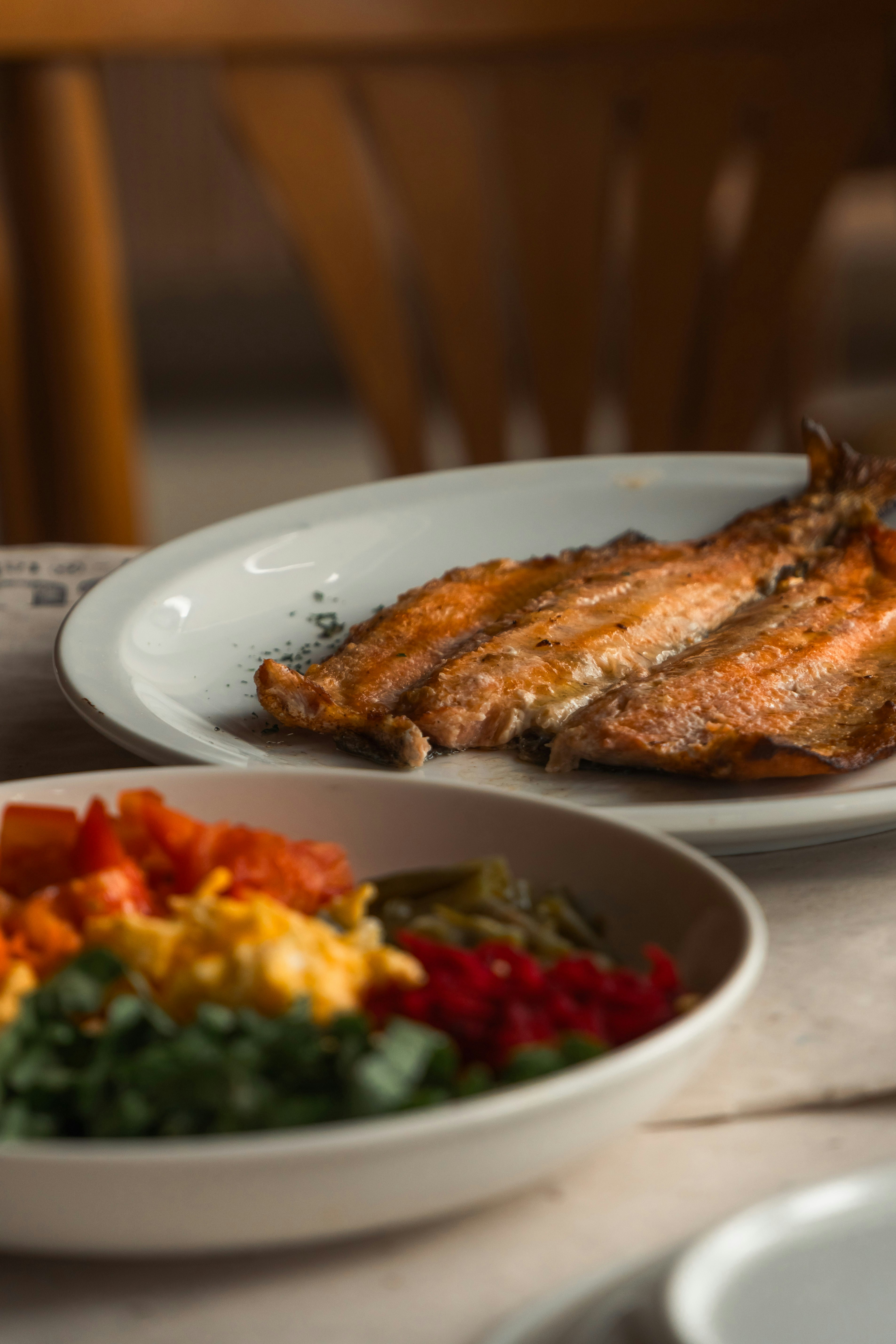 A plate of grilled fish beside a bowl of chopped vegetables on a table