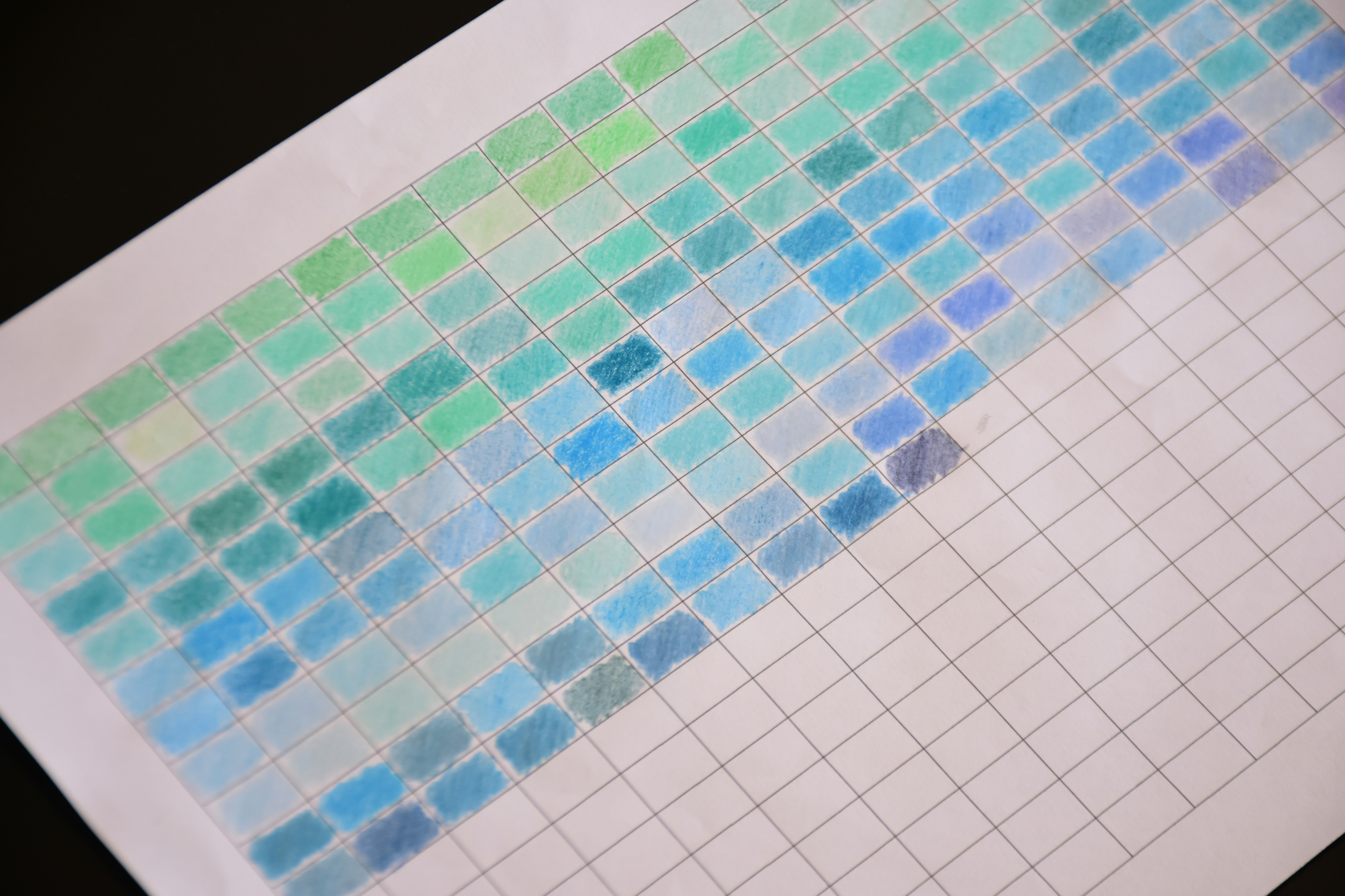A grid of hand-drawn color swatches transitioning from green to blue on white paper