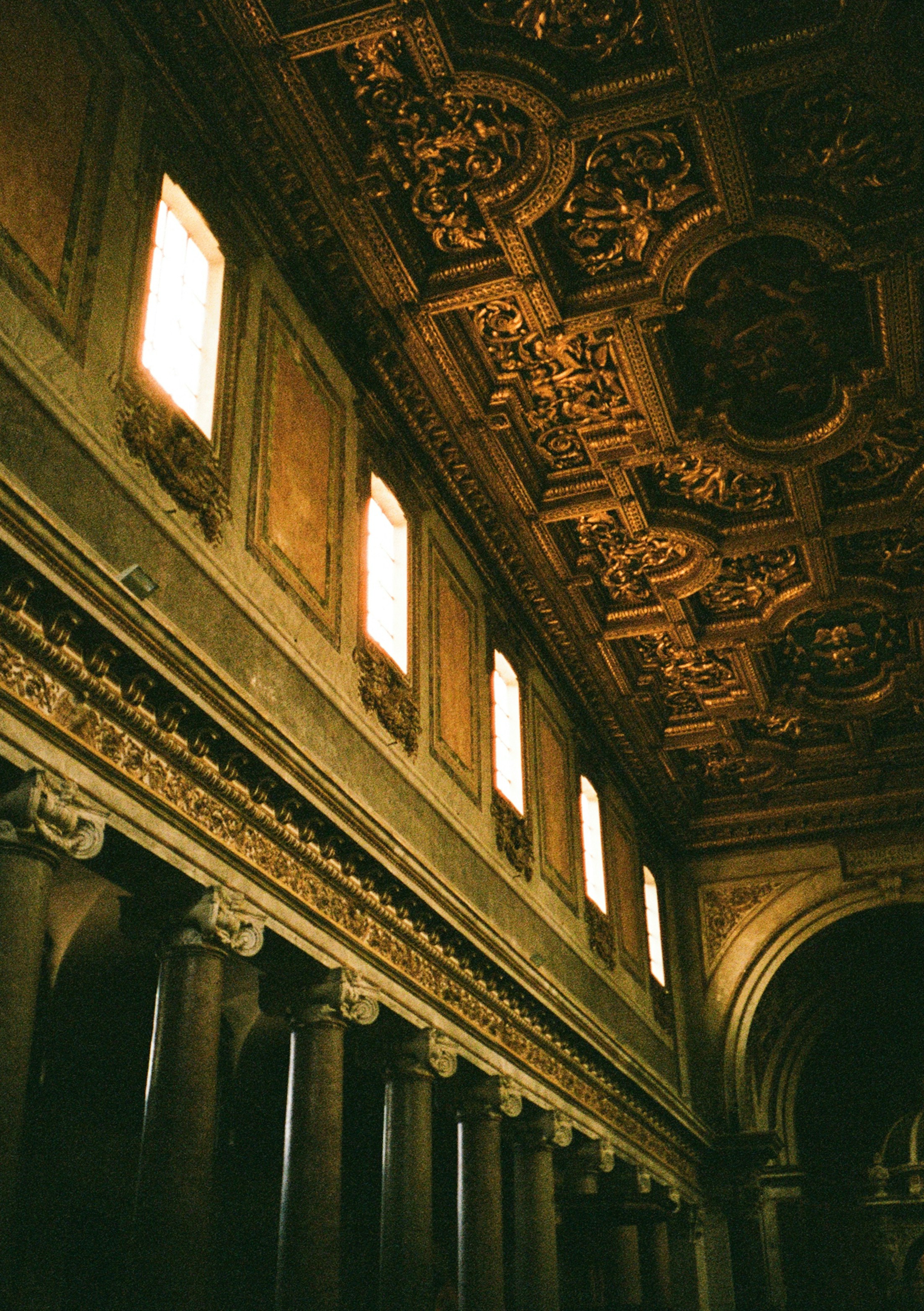 Ornate gold ceiling and stone columns in a sunlit church interior in Rome