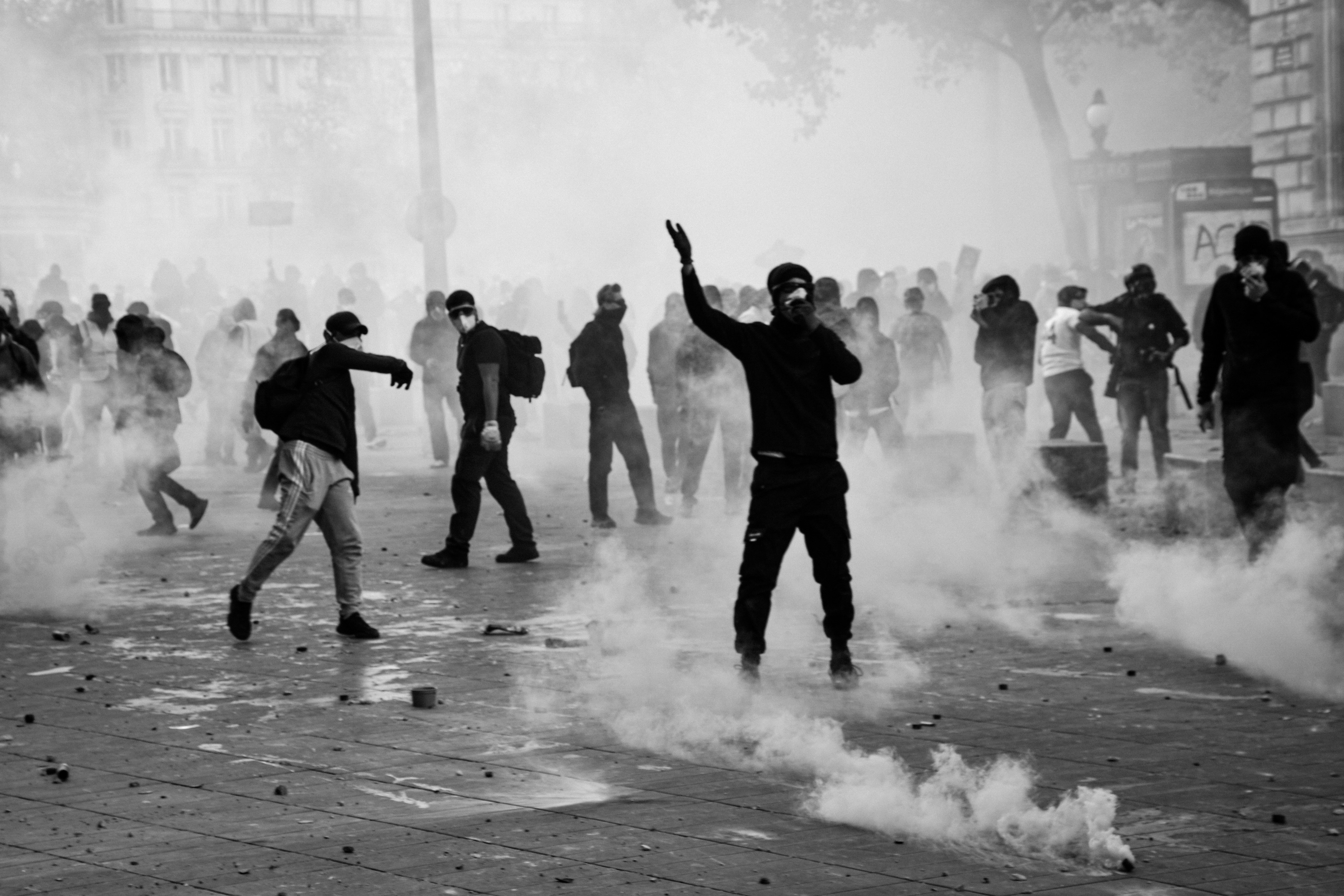 People in dark clothing moving through thick smoke on a city street in black and white