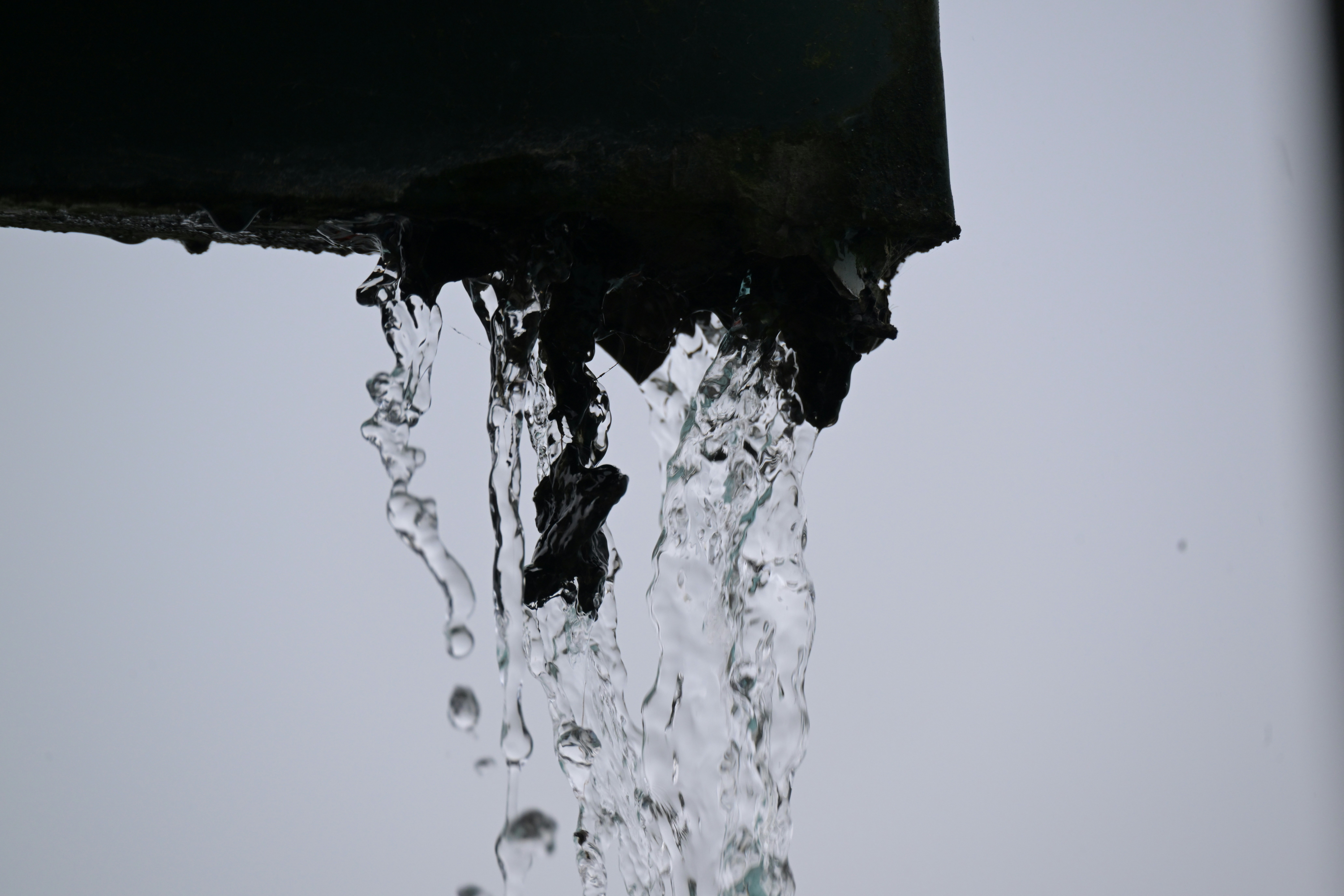 Rainwater pouring from the corner of a dark metal gutter