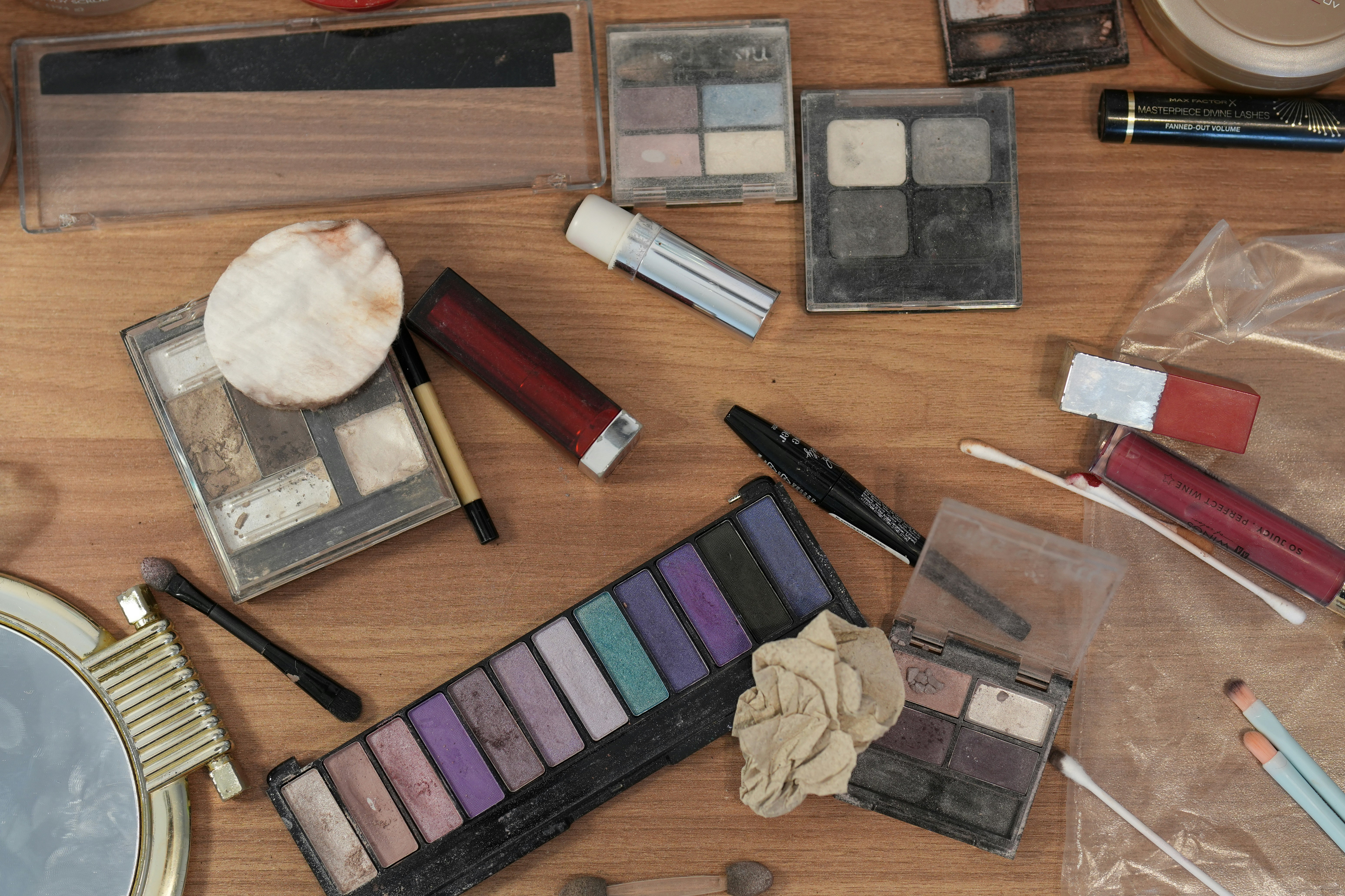 An assortment of makeup palettes, lipsticks, and brushes scattered on a wooden surface