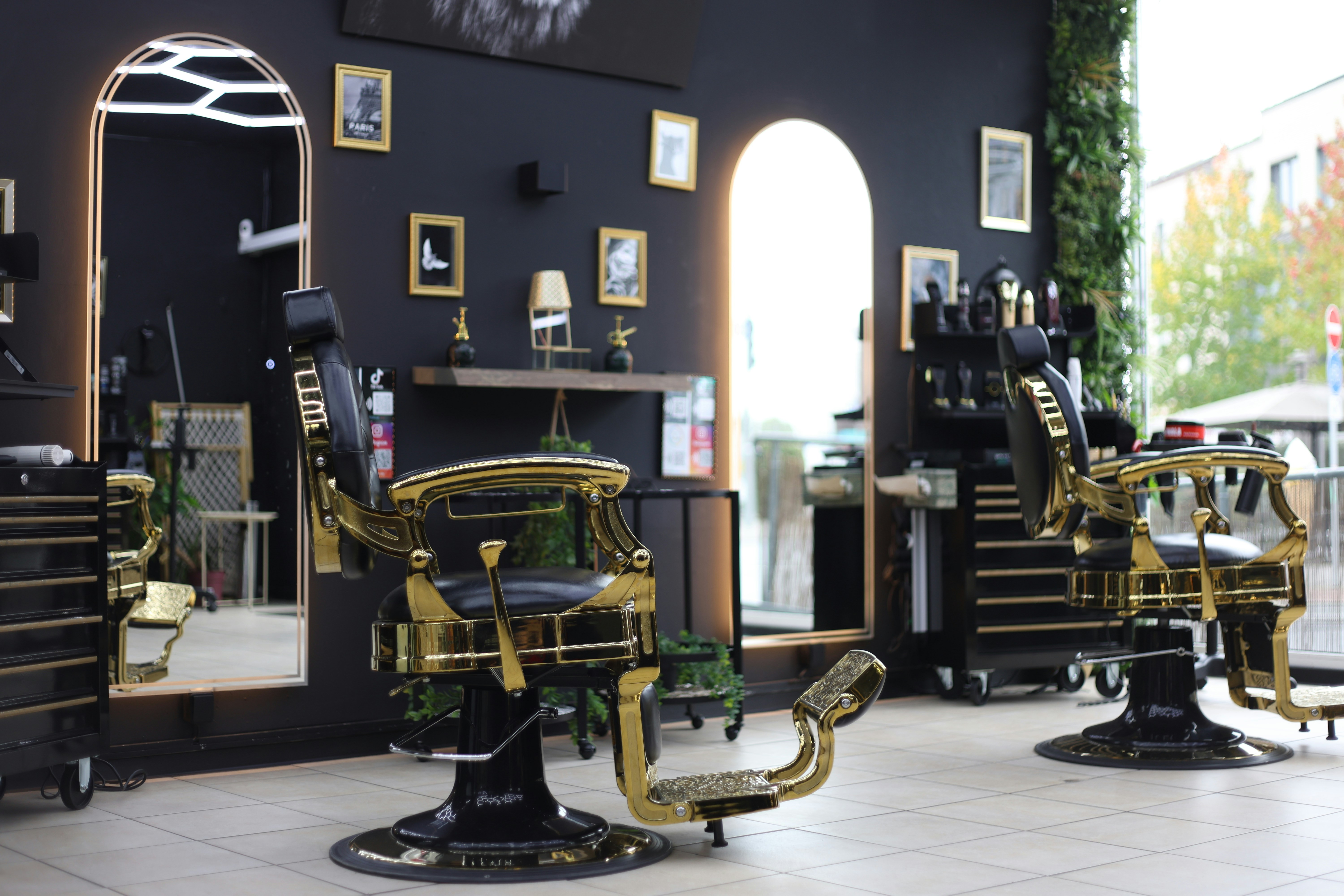 Two ornate black and gold barber chairs in a modern salon with arched mirrors