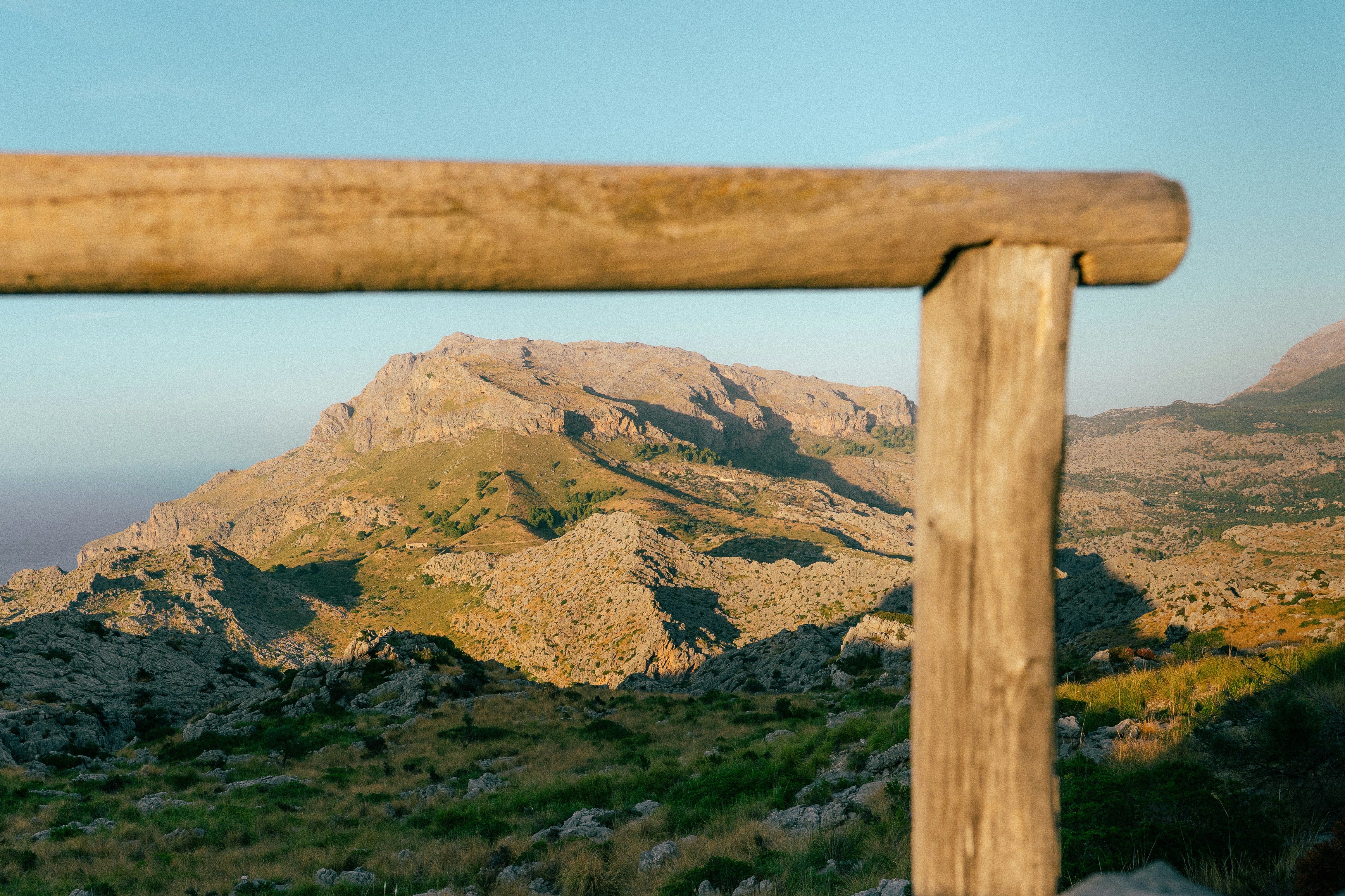 A rocky mountain landscape viewed through a wooden fence rail in warm light