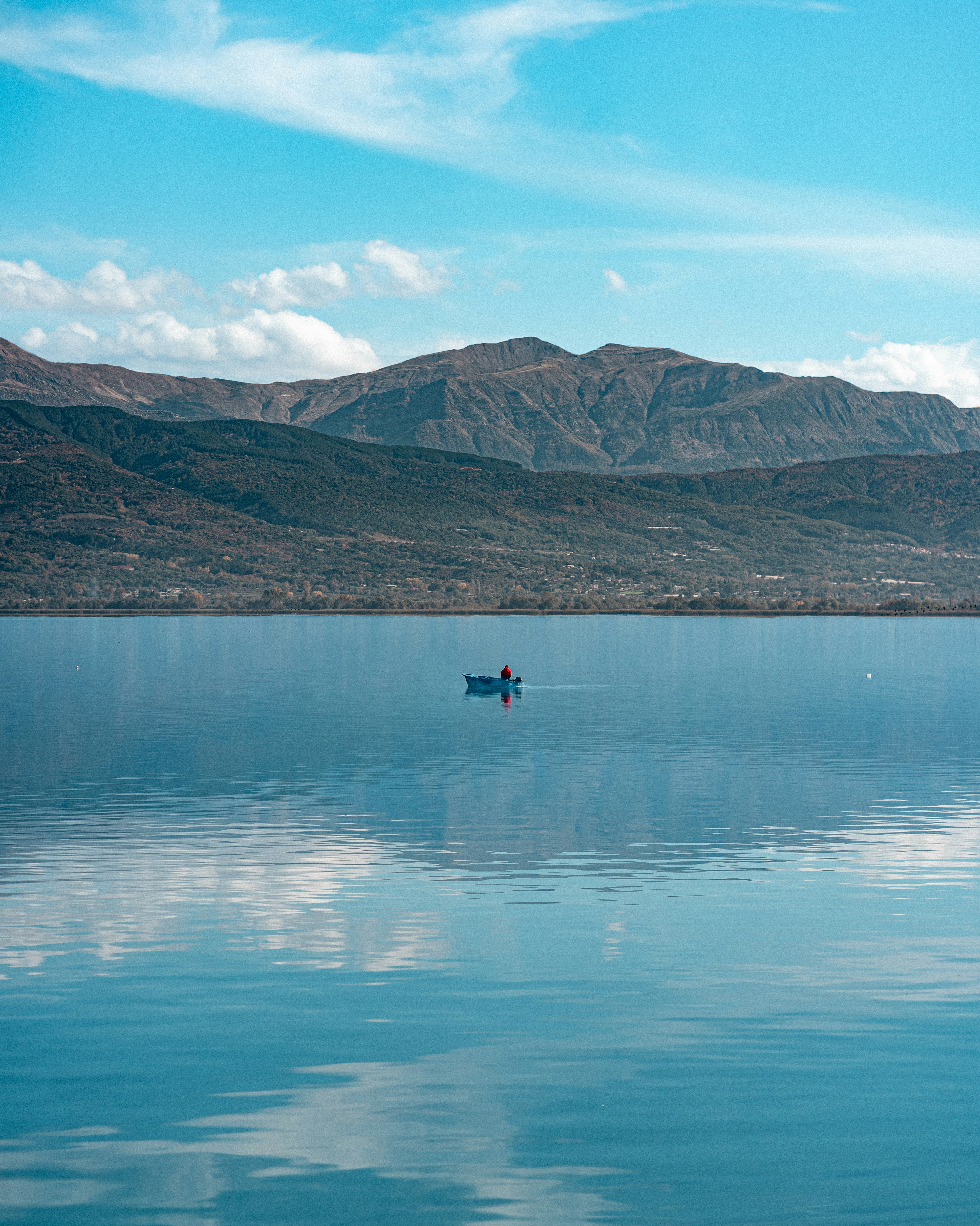 A person in a small boat on a calm lake beneath distant mountains
