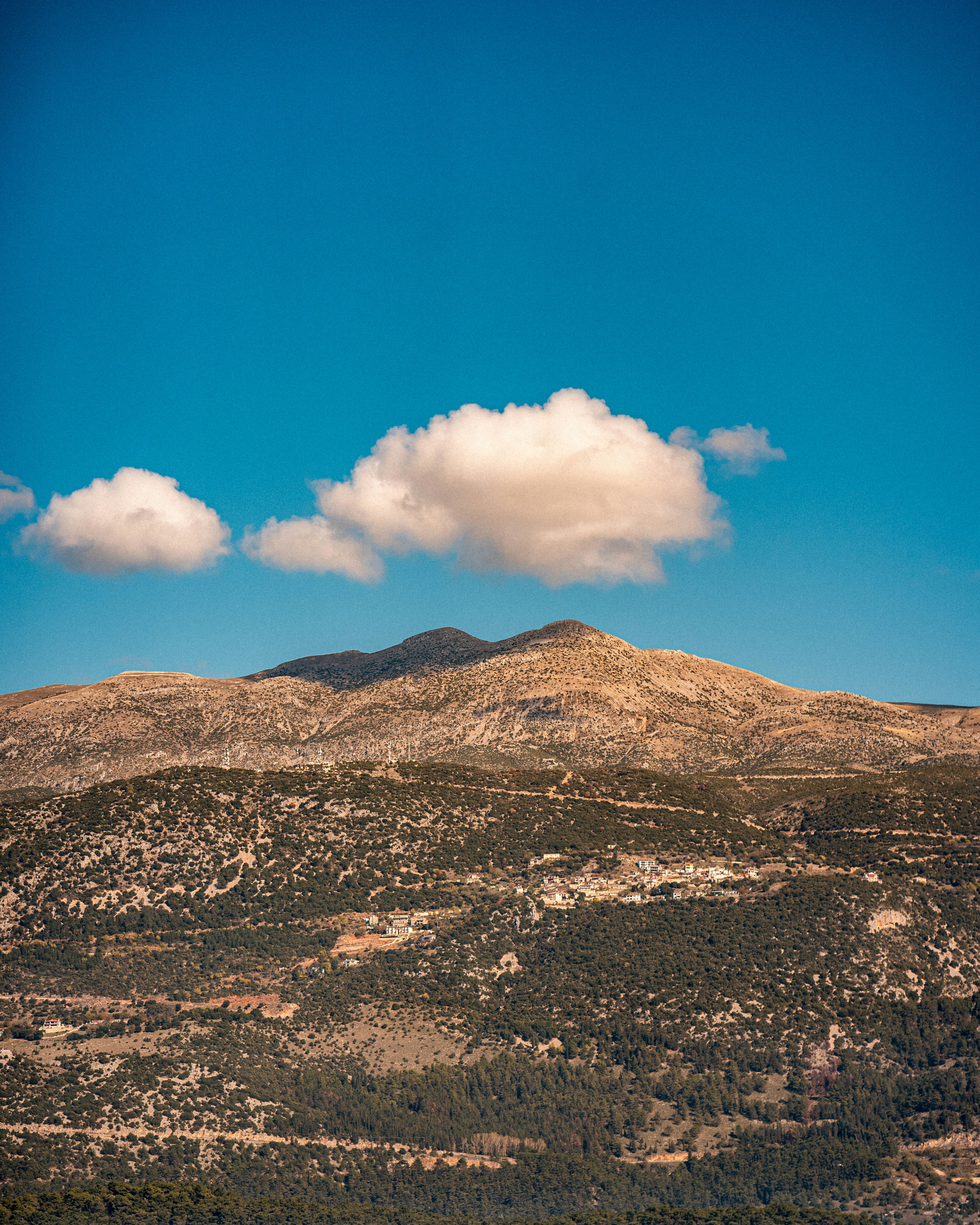 A mountain range with sparse vegetation and a small village under a clear blue sky