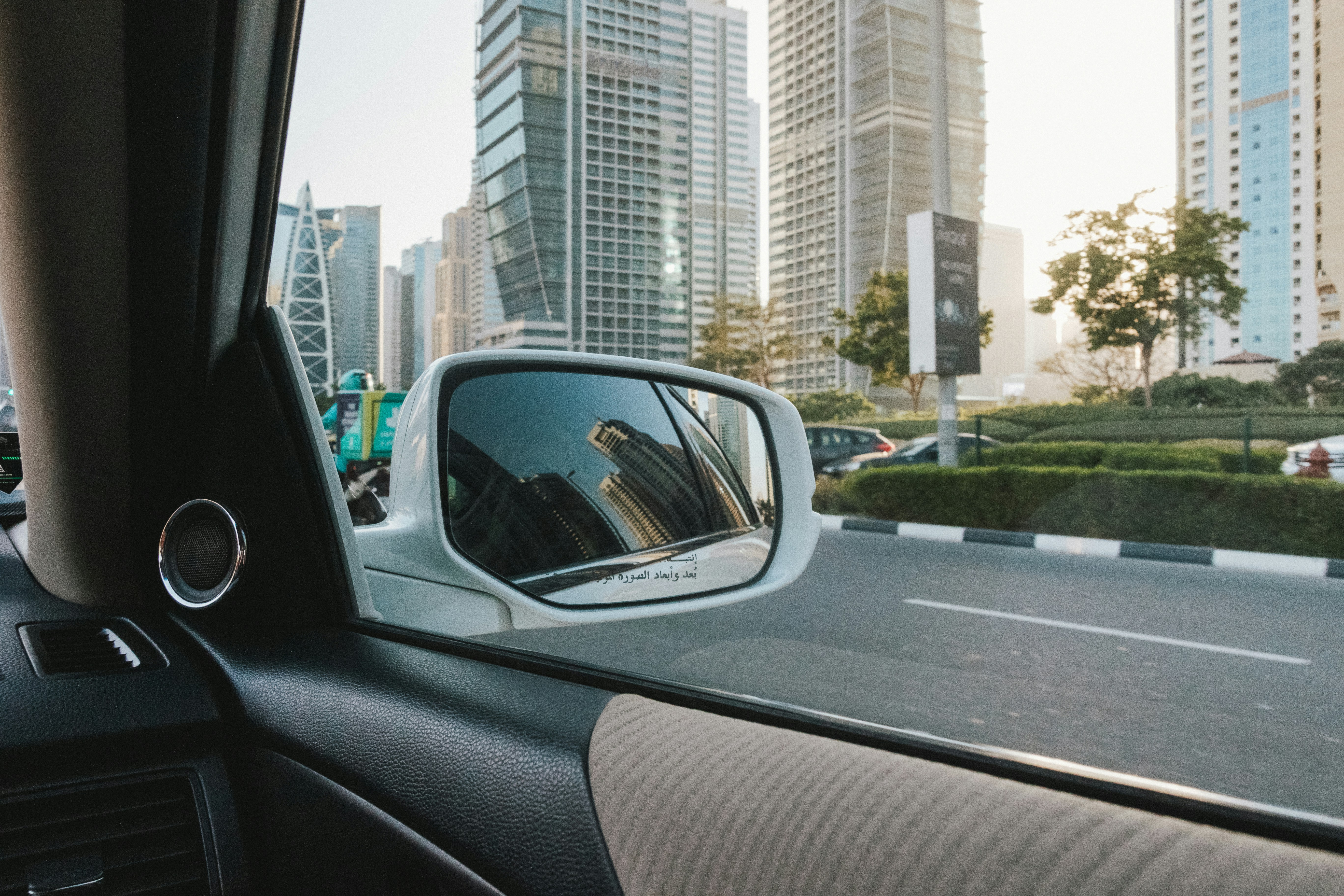 A view from inside a car showing skyscrapers reflected in the side mirror