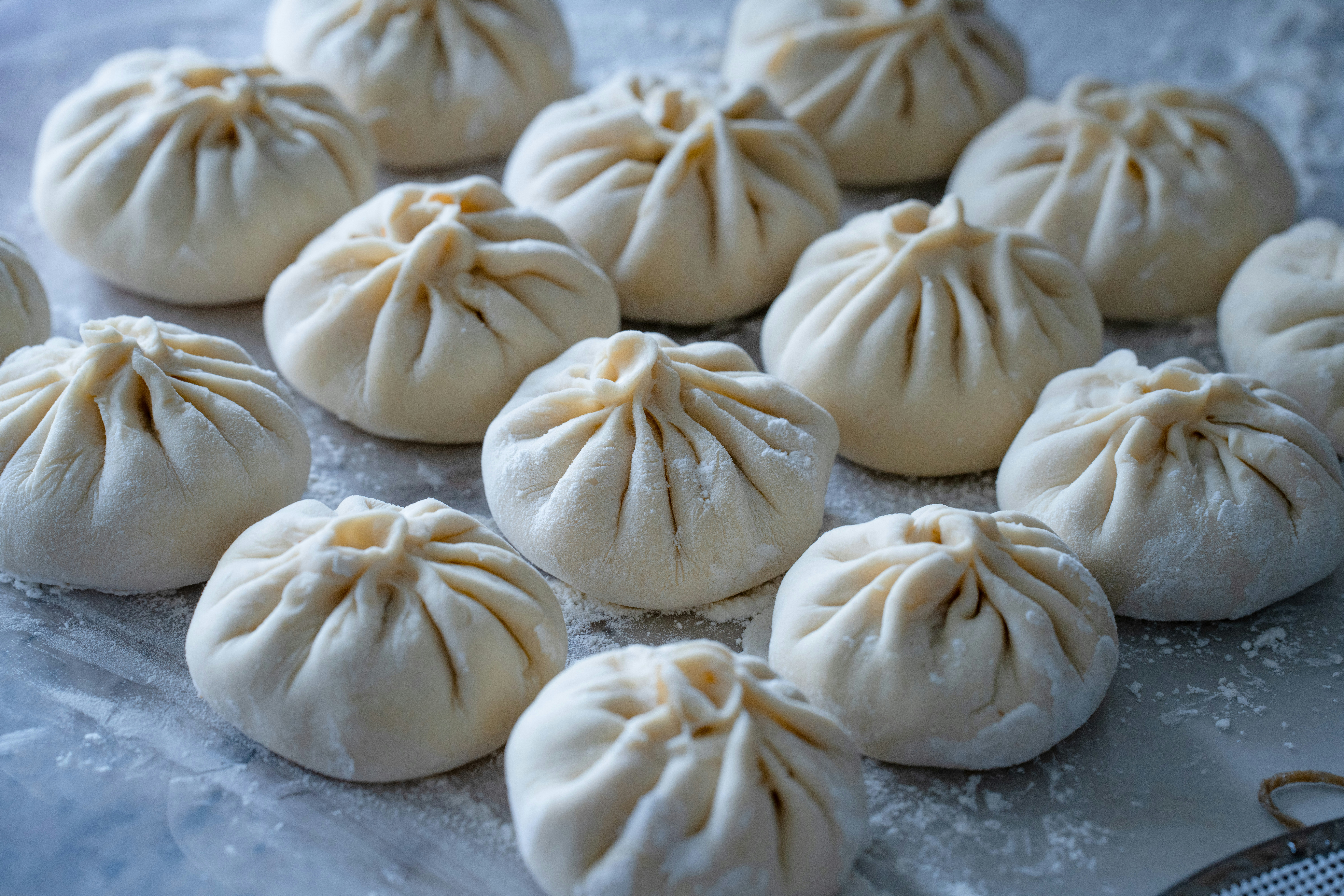 Many raw pleated dough dumplings arranged on a floured surface