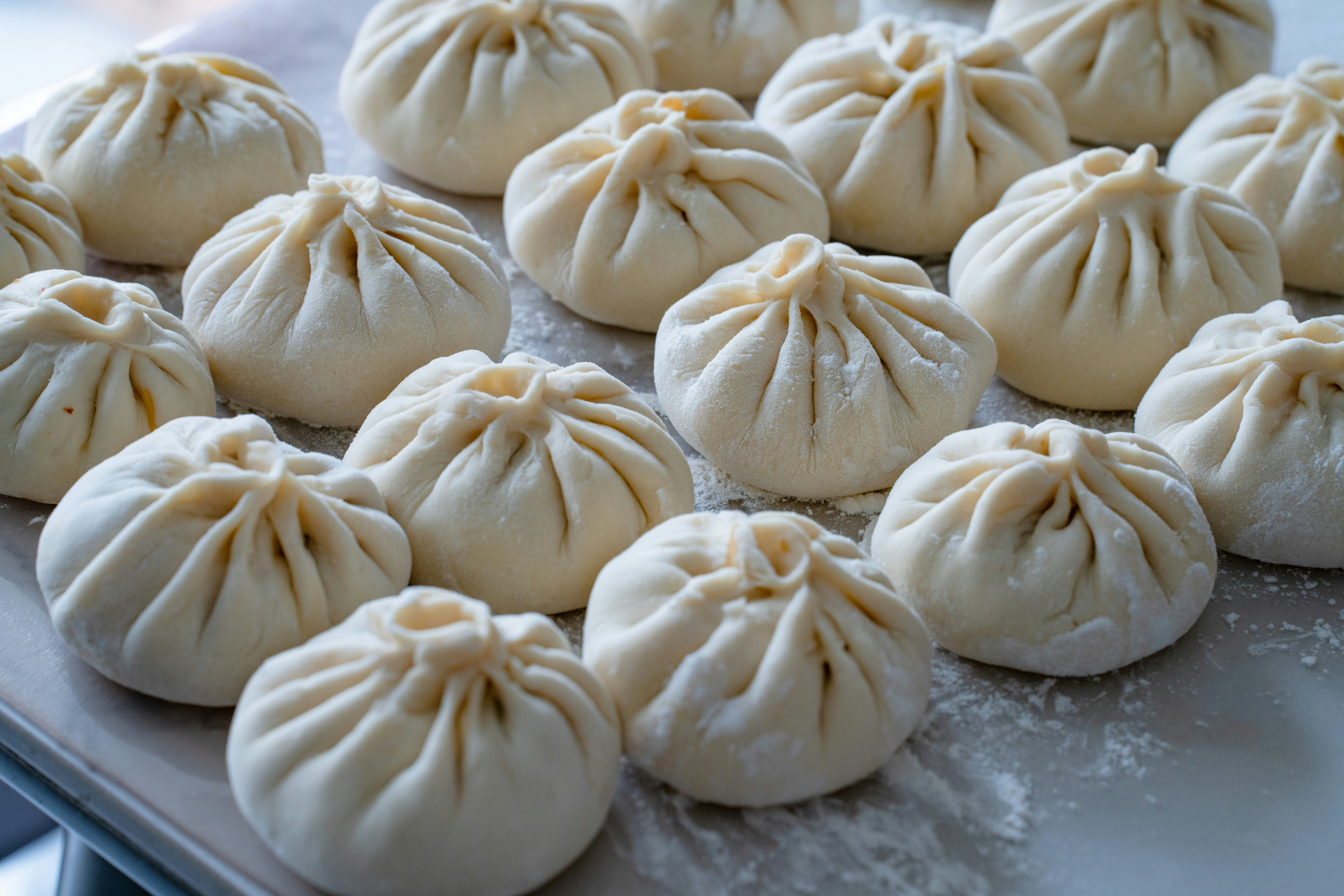 Many raw pleated dumplings arranged on a floured surface