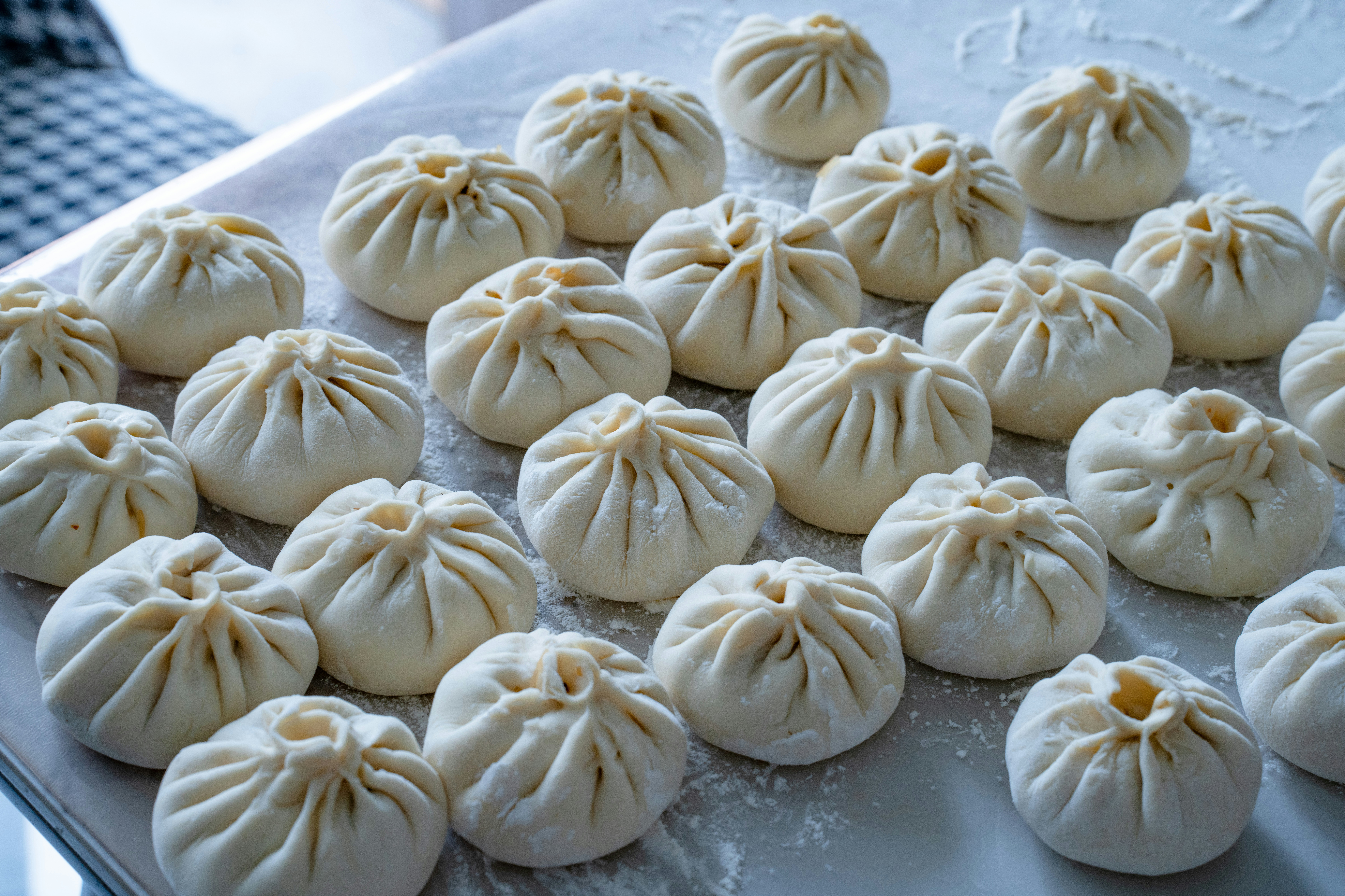 Many raw pleated dough buns arranged on a floured surface for cooking