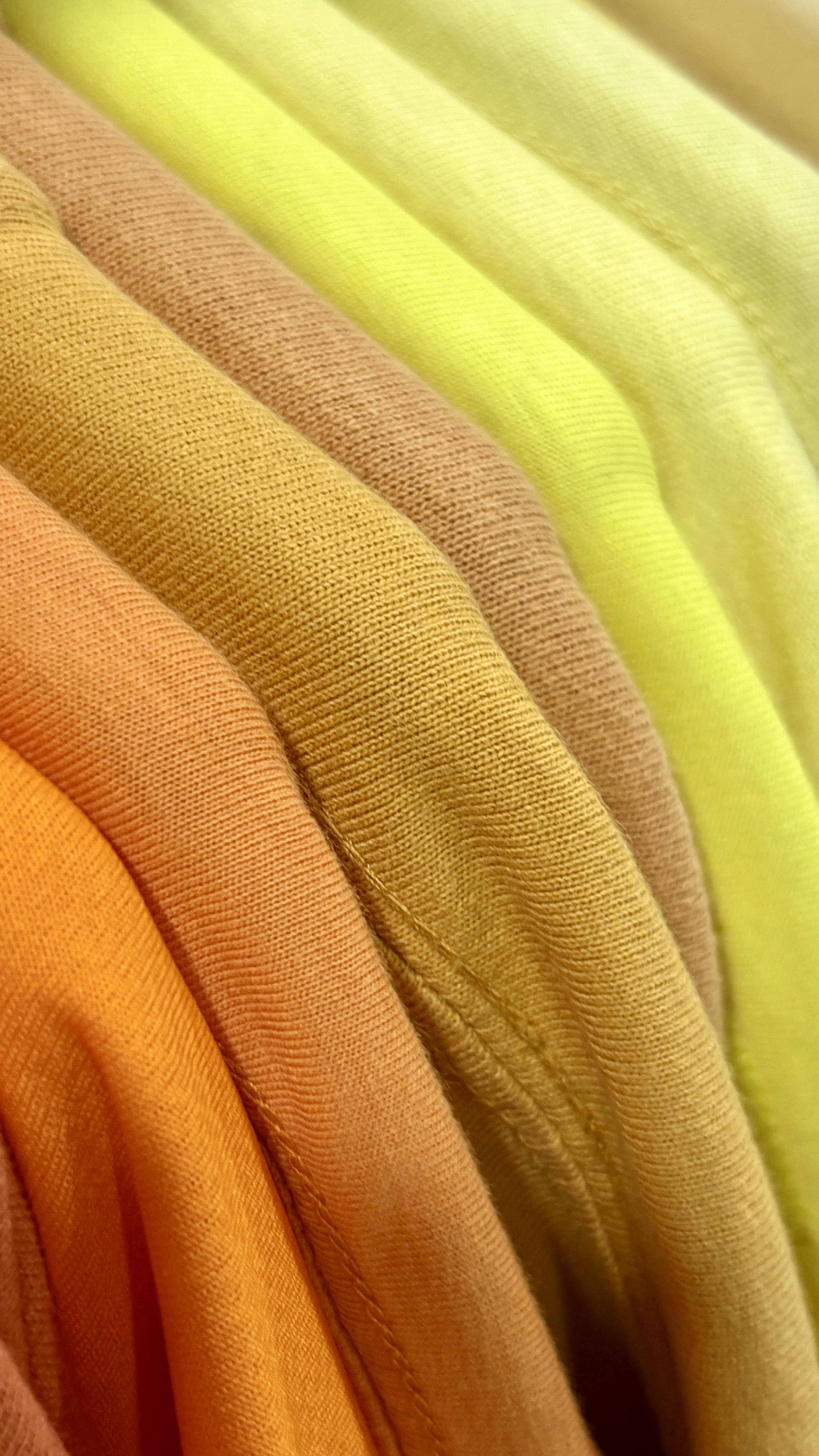 Fotomural A stack of folded t-shirts in a gradient of orange, tan, and yellow