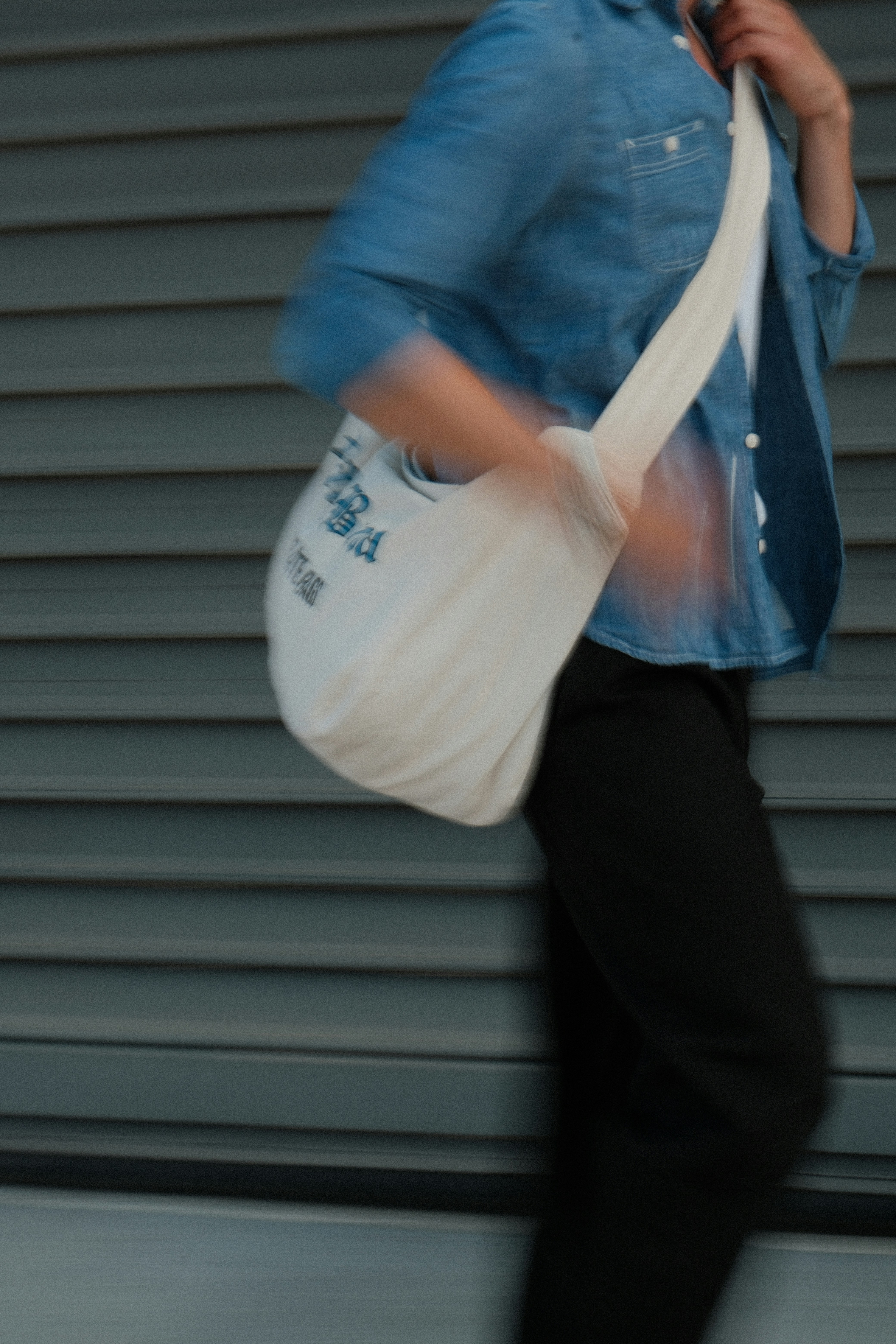 A person in a denim shirt and black trousers walking with a white canvas bag - 相关推荐