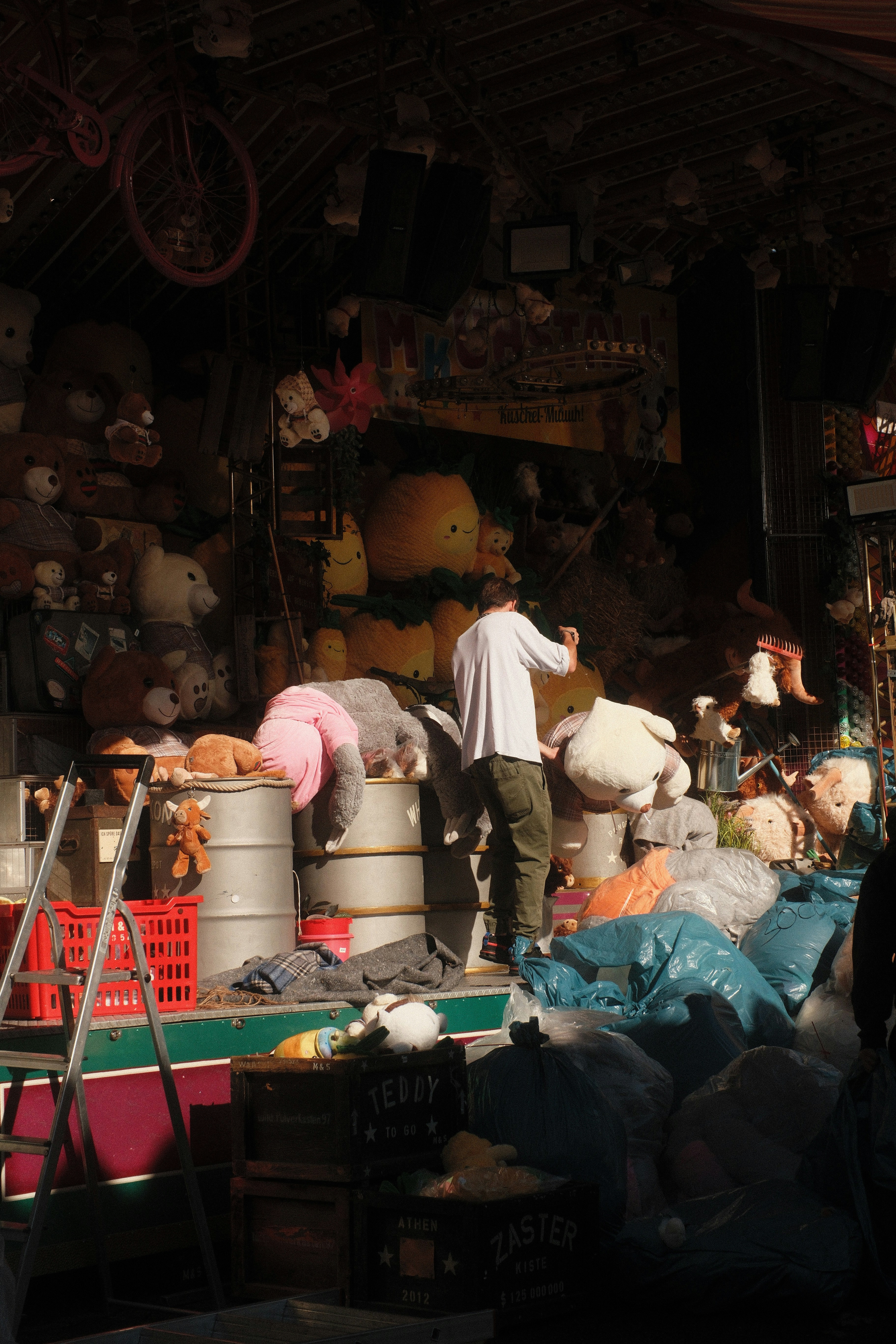 A person arranging plush toys on metal barrels at a carnival game stall