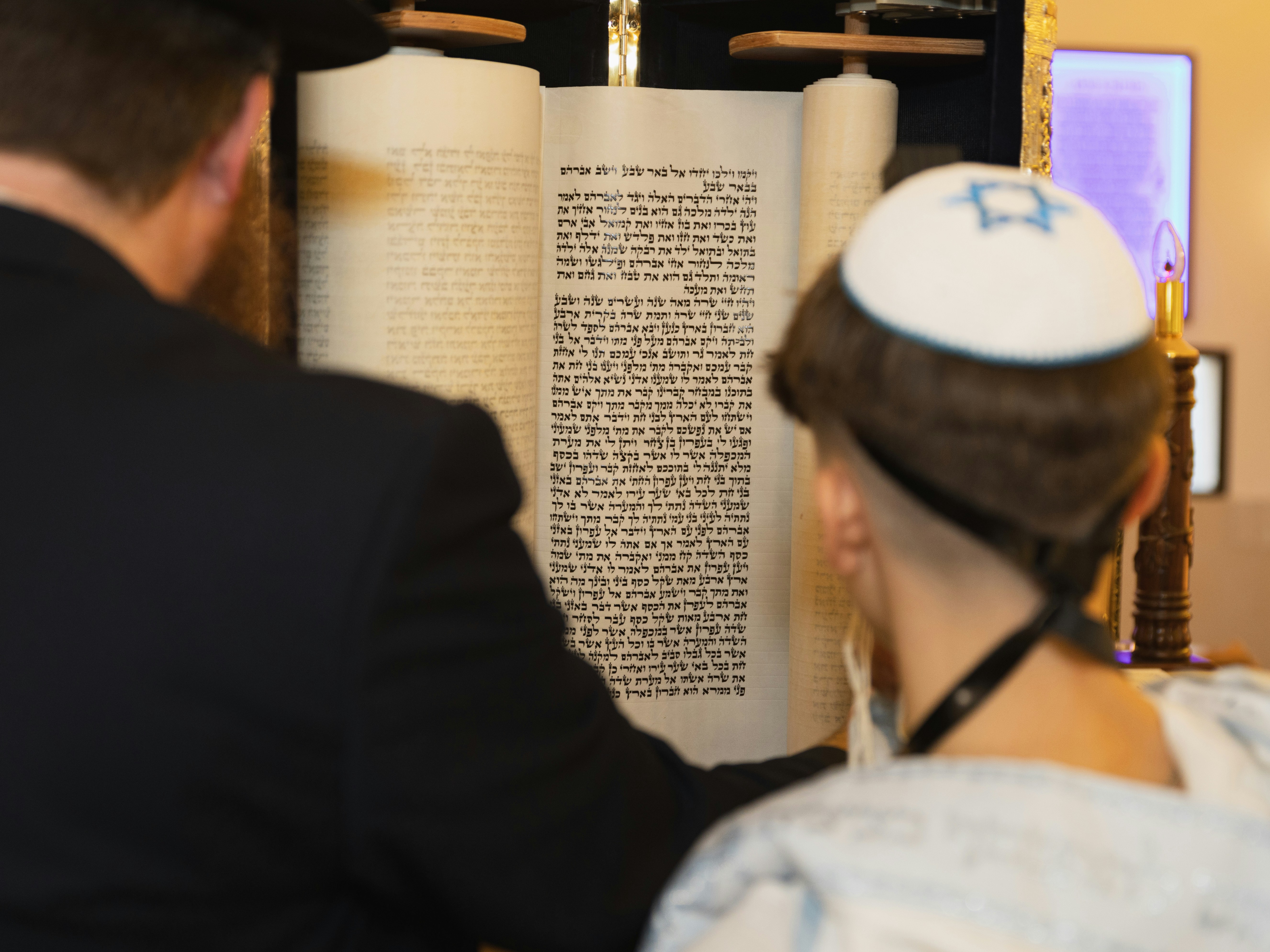 An adult and a child reading from an open Torah scroll in a synagogue
