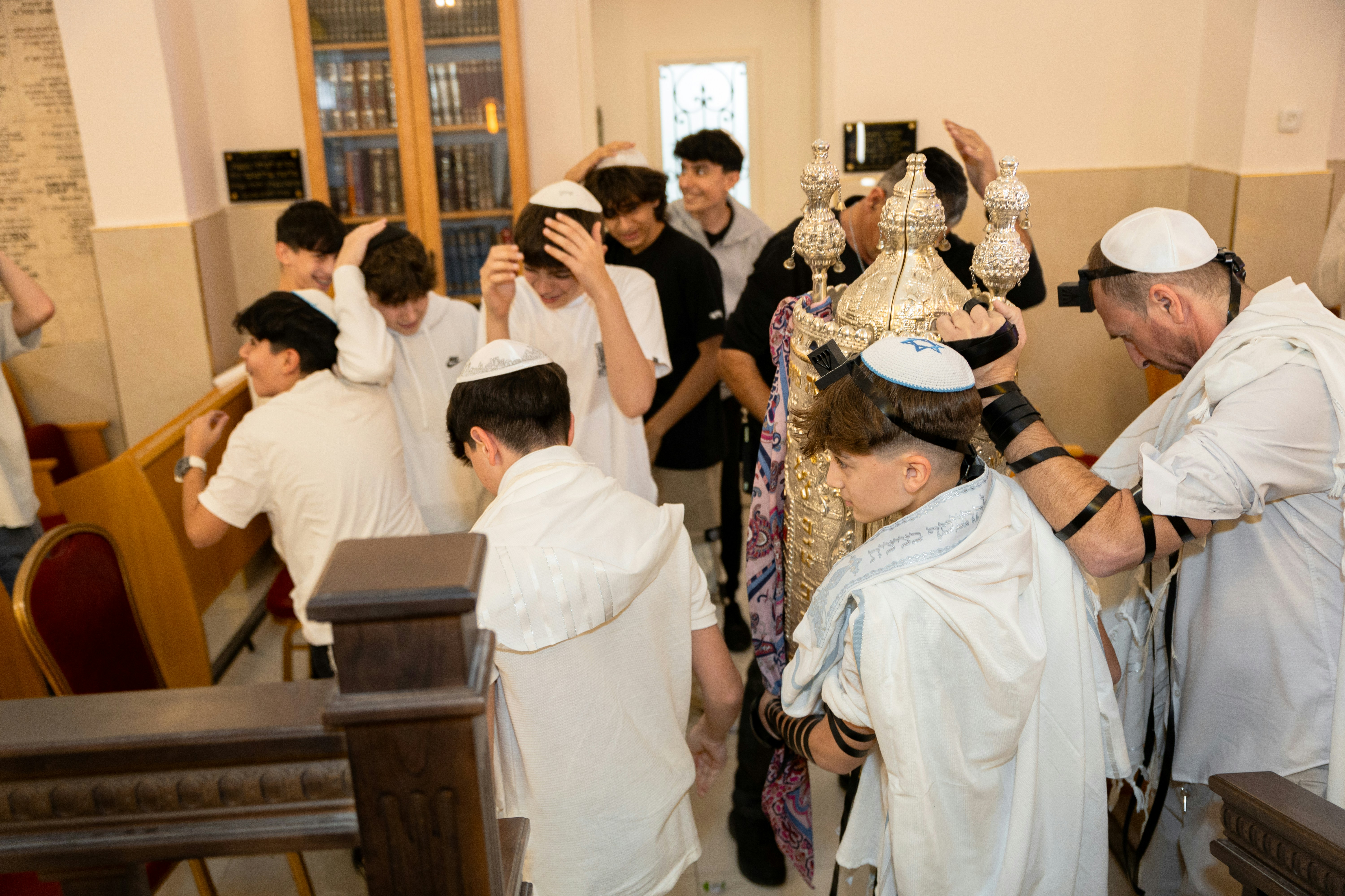 A group of people in a synagogue surrounding a person holding a silver Torah scroll