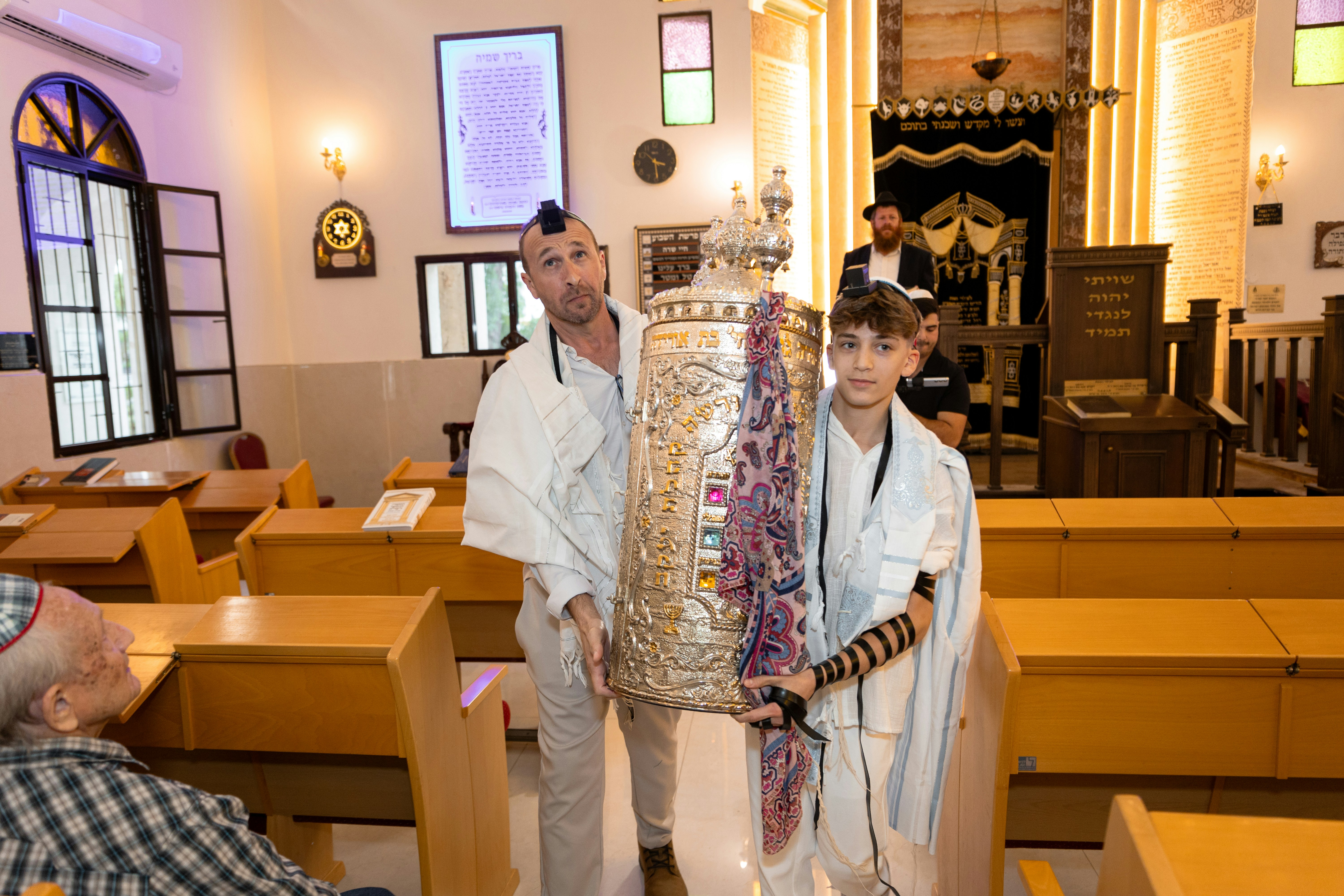 An adult and a boy carrying a silver Torah scroll in a synagogue