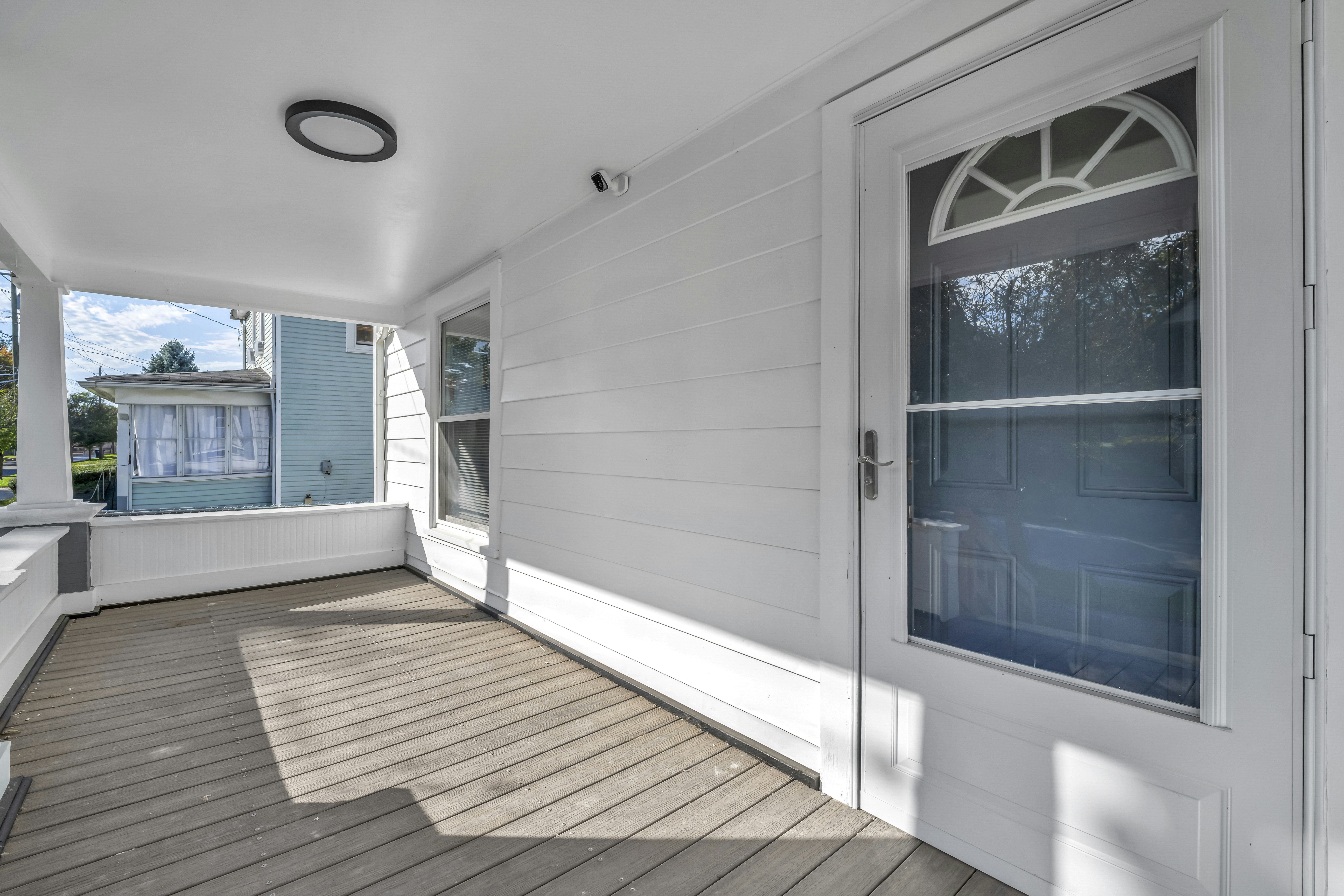 A white front porch with a wooden floor and a glass panel door