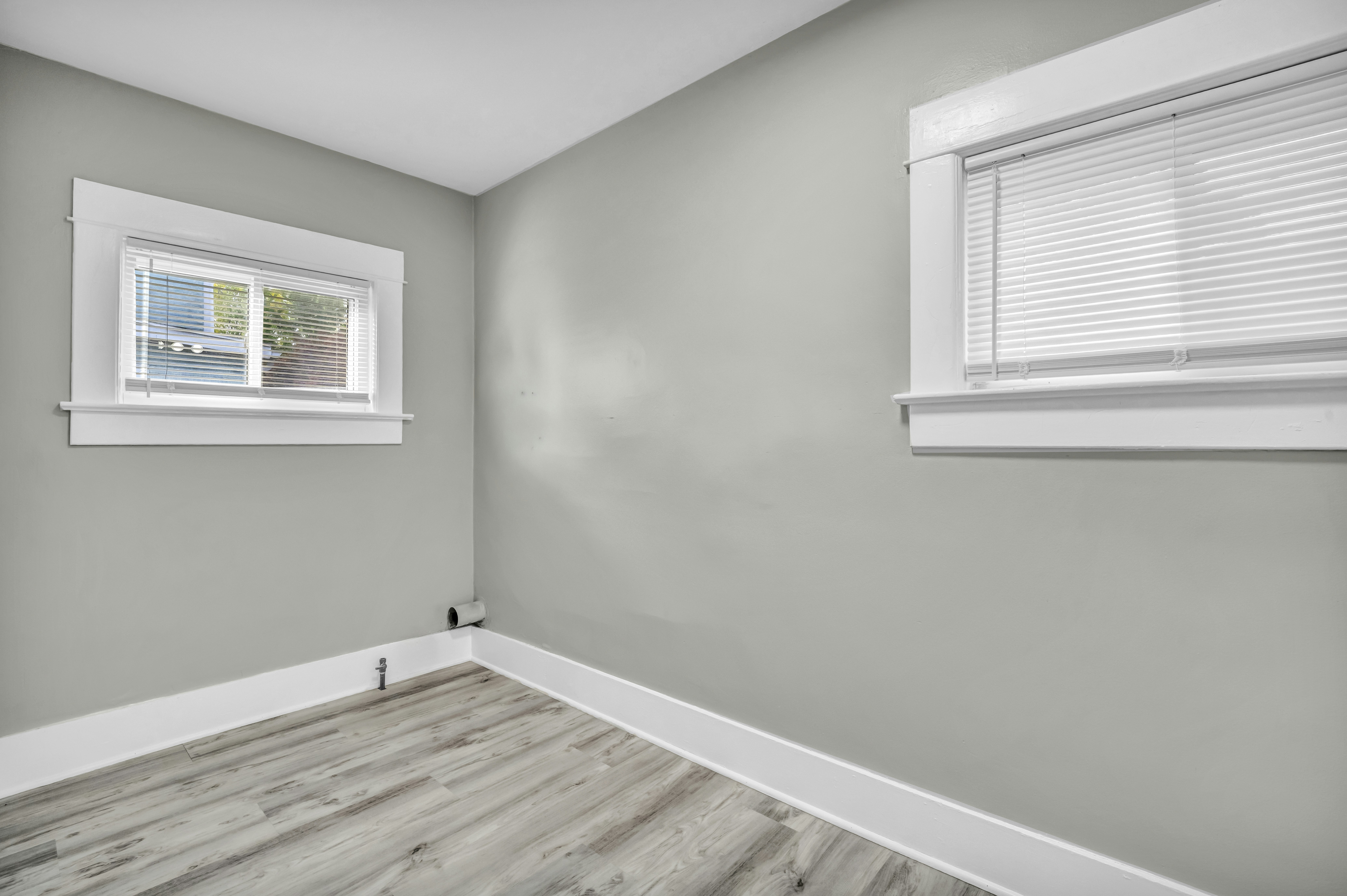 An empty room with light grey walls, white trim, and wood-look flooring
