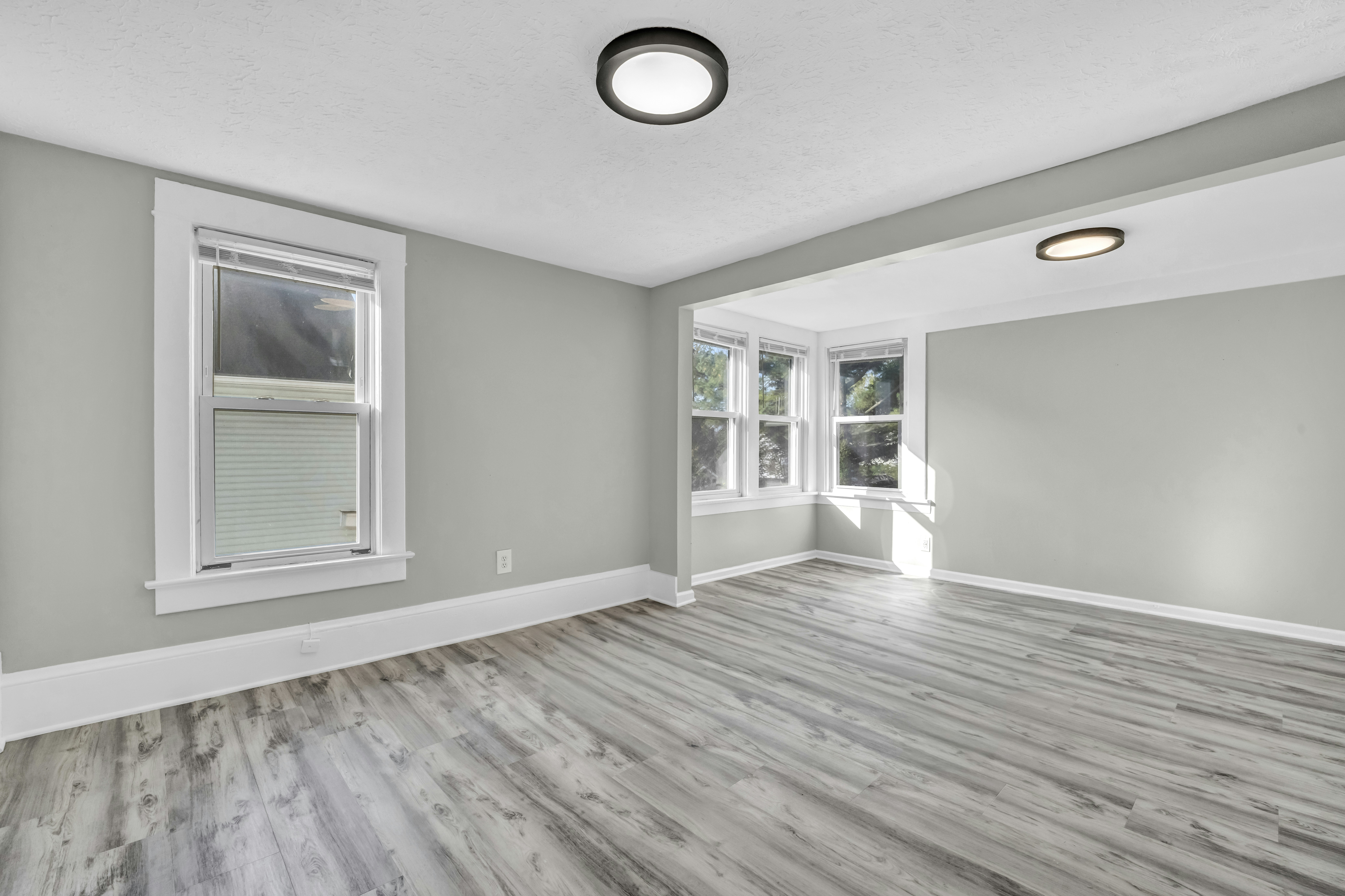 An empty room with light grey walls, white trim and grey wood-look flooring