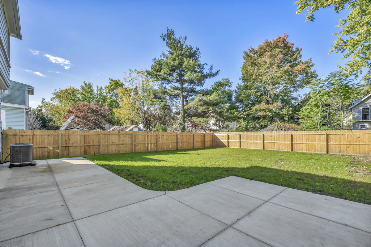 Concrete patio beside a green lawn and a tall wooden privacy fence