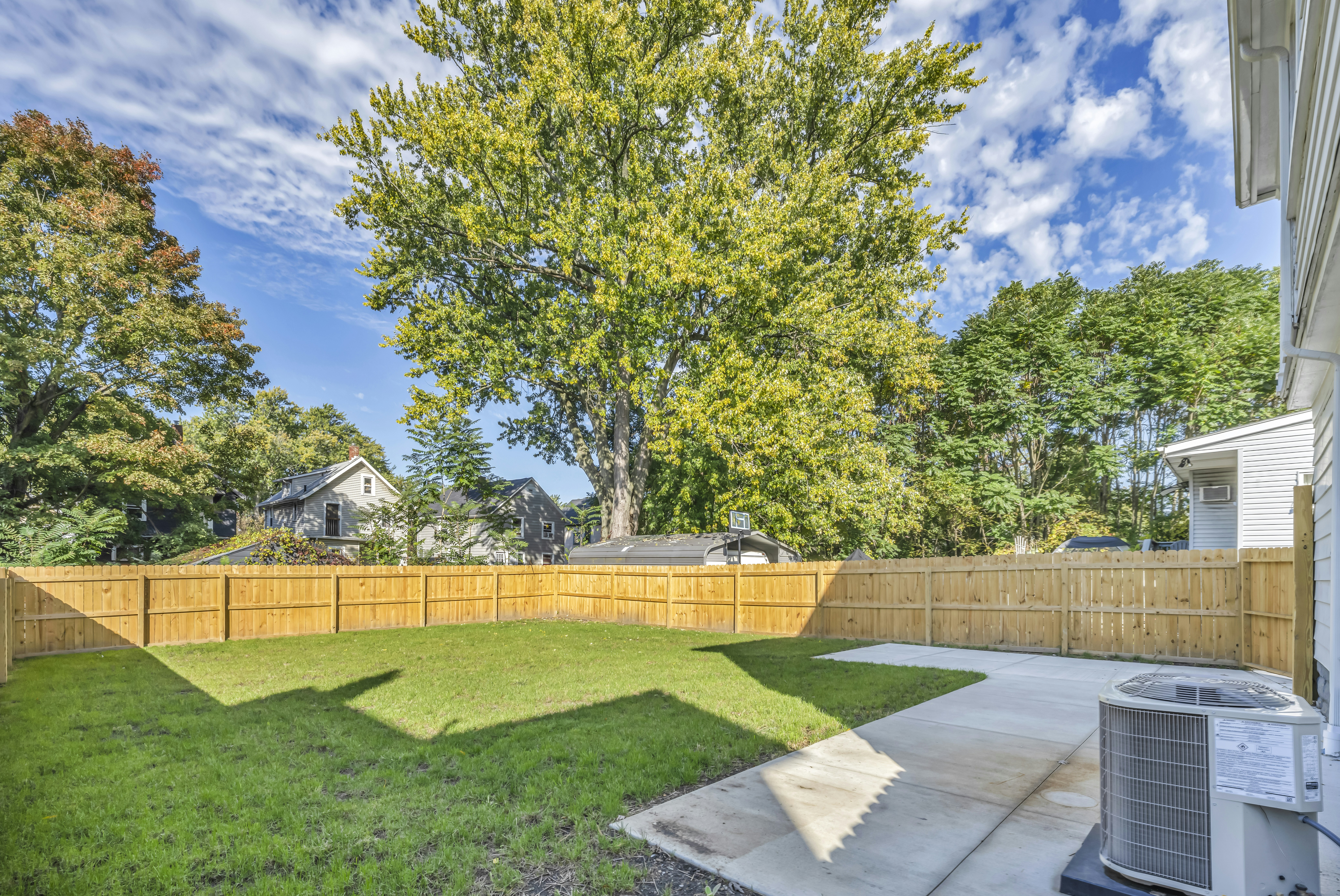 Fenced backyard with a green lawn, patio and large tree