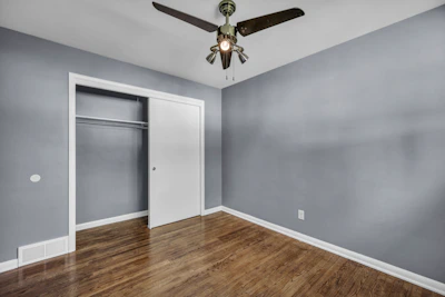 An empty bedroom with grey walls, hardwood floors, and a white sliding closet door