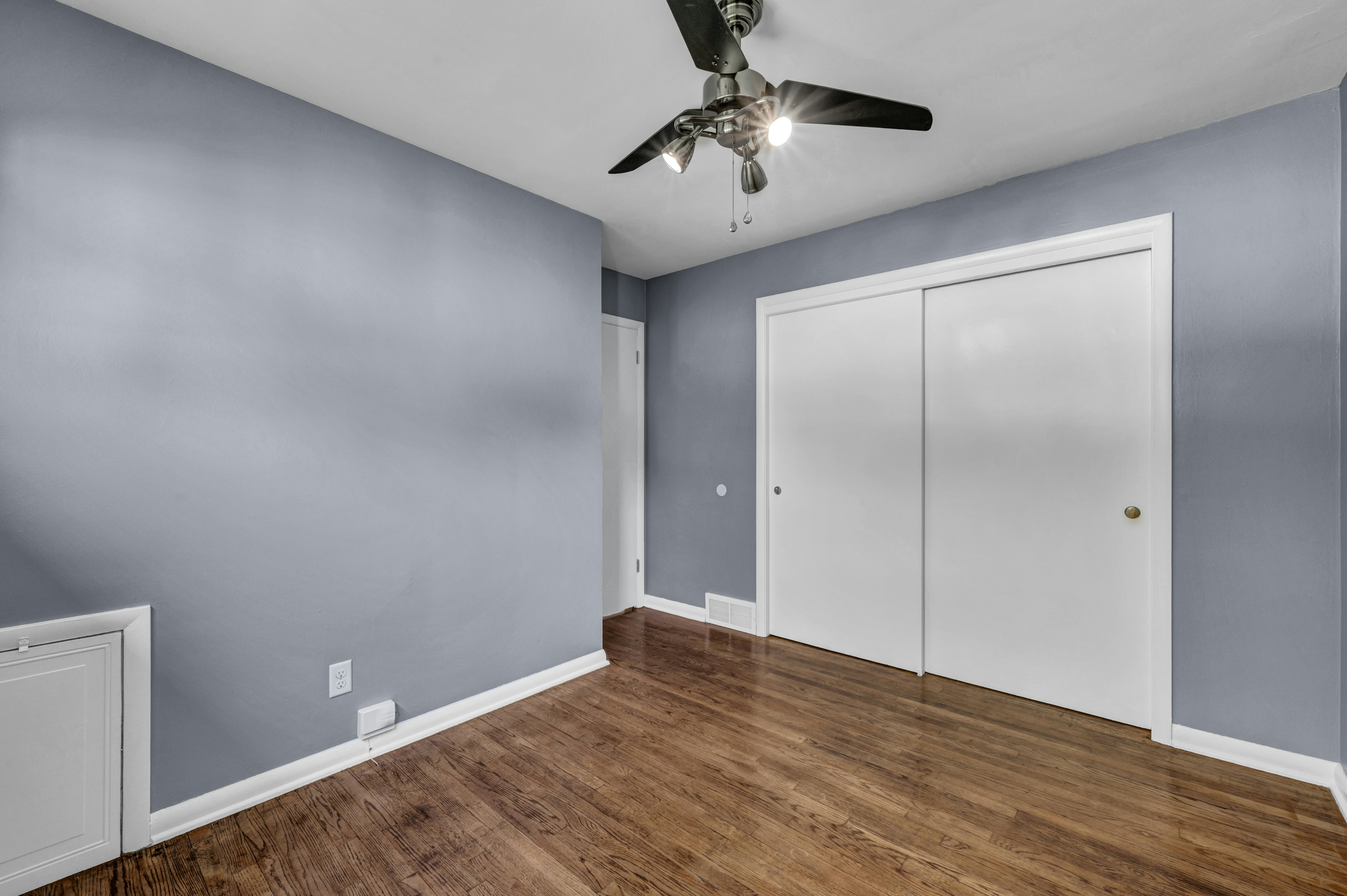 An empty room with blue walls, white sliding closet doors, and dark hardwood flooring