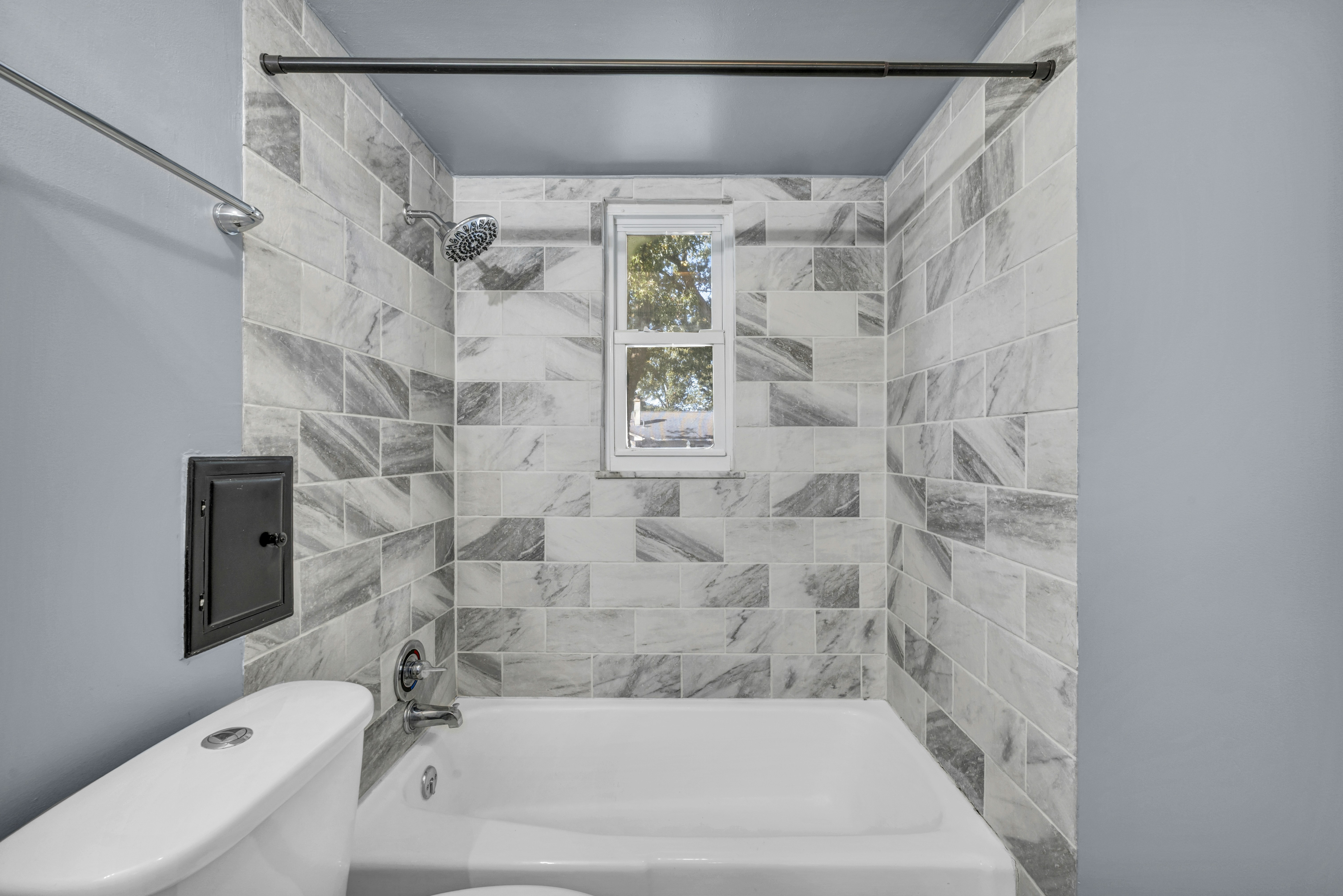 Baignoire et douche fraîchement carrelées en carreaux effet marbre gris et blanc, avec petite fenêtre et niche