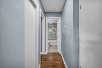 A narrow hallway with light blue walls and wooden flooring leading to a bathroom