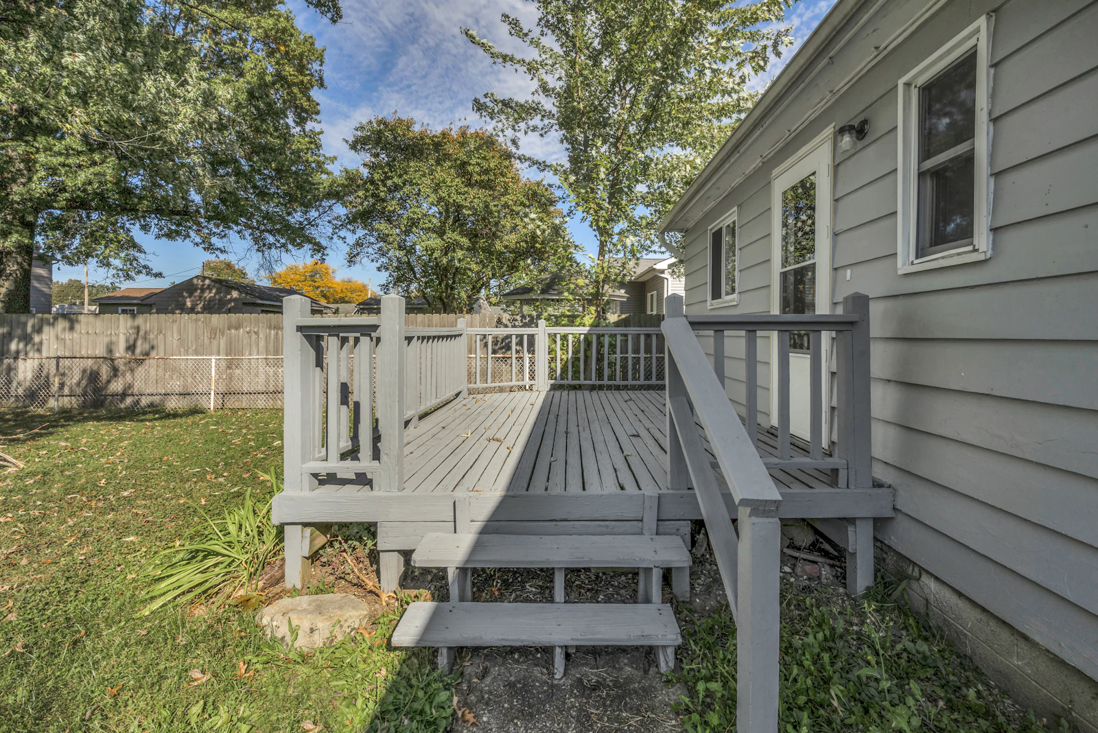 Gray painted wood deck with railings and steps off the back of a house