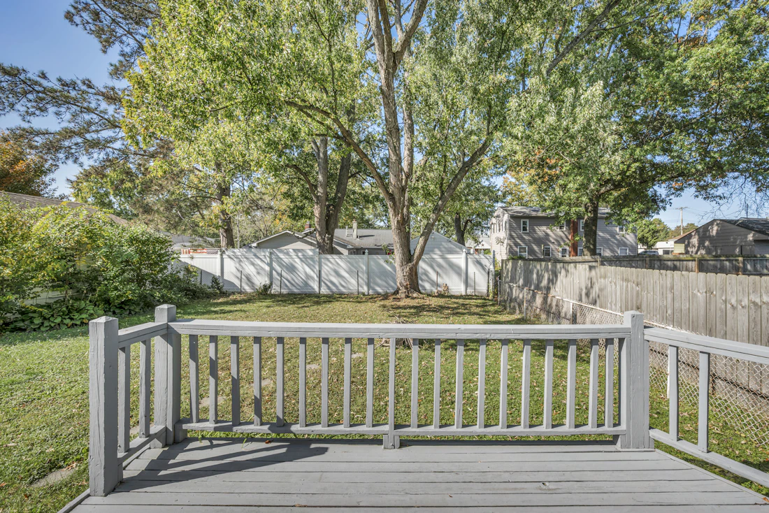 View from a wooden deck over a fenced backyard with large trees