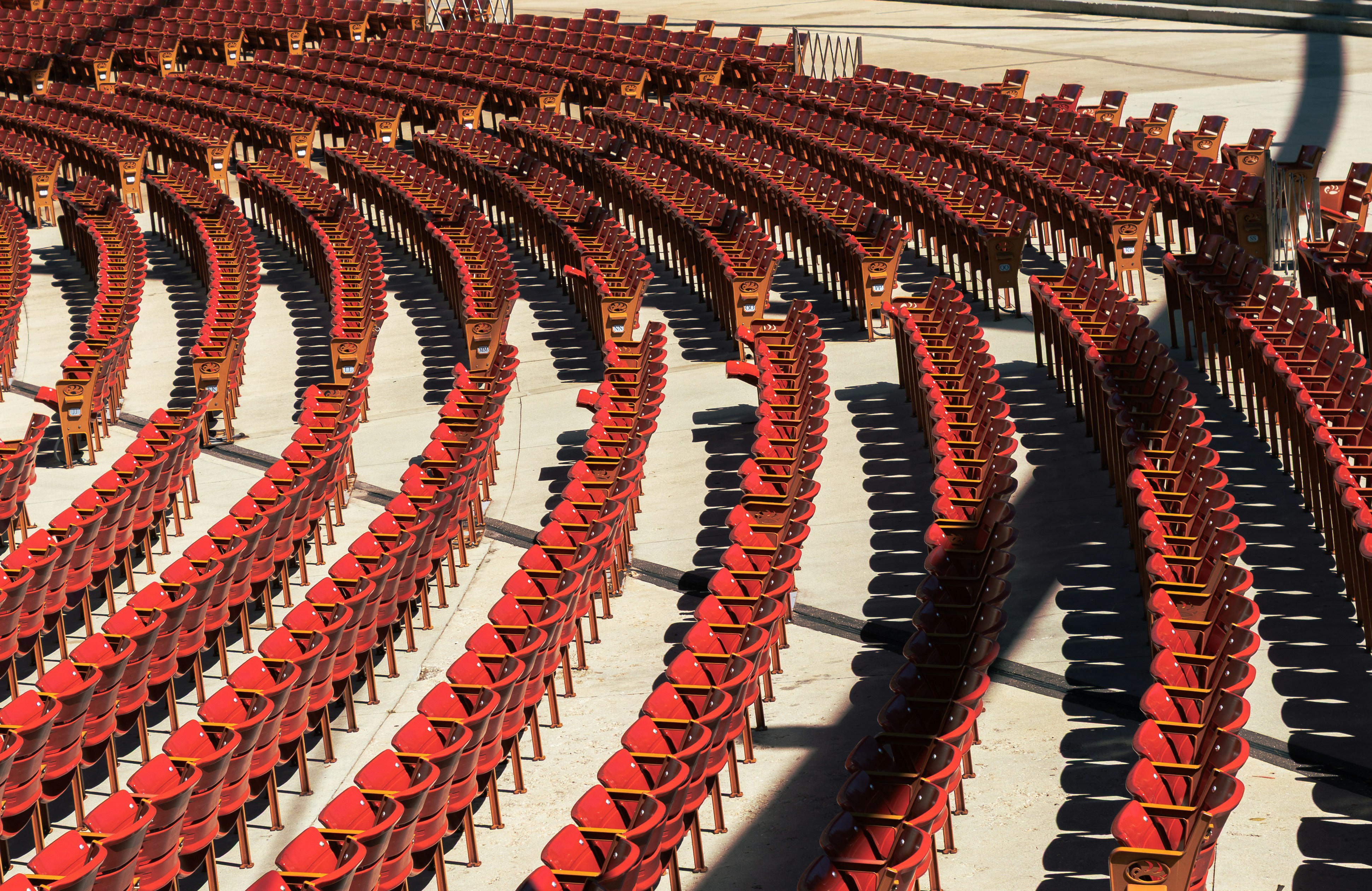 Rows of empty red stadium seats arranged in curved sections on a concrete floor