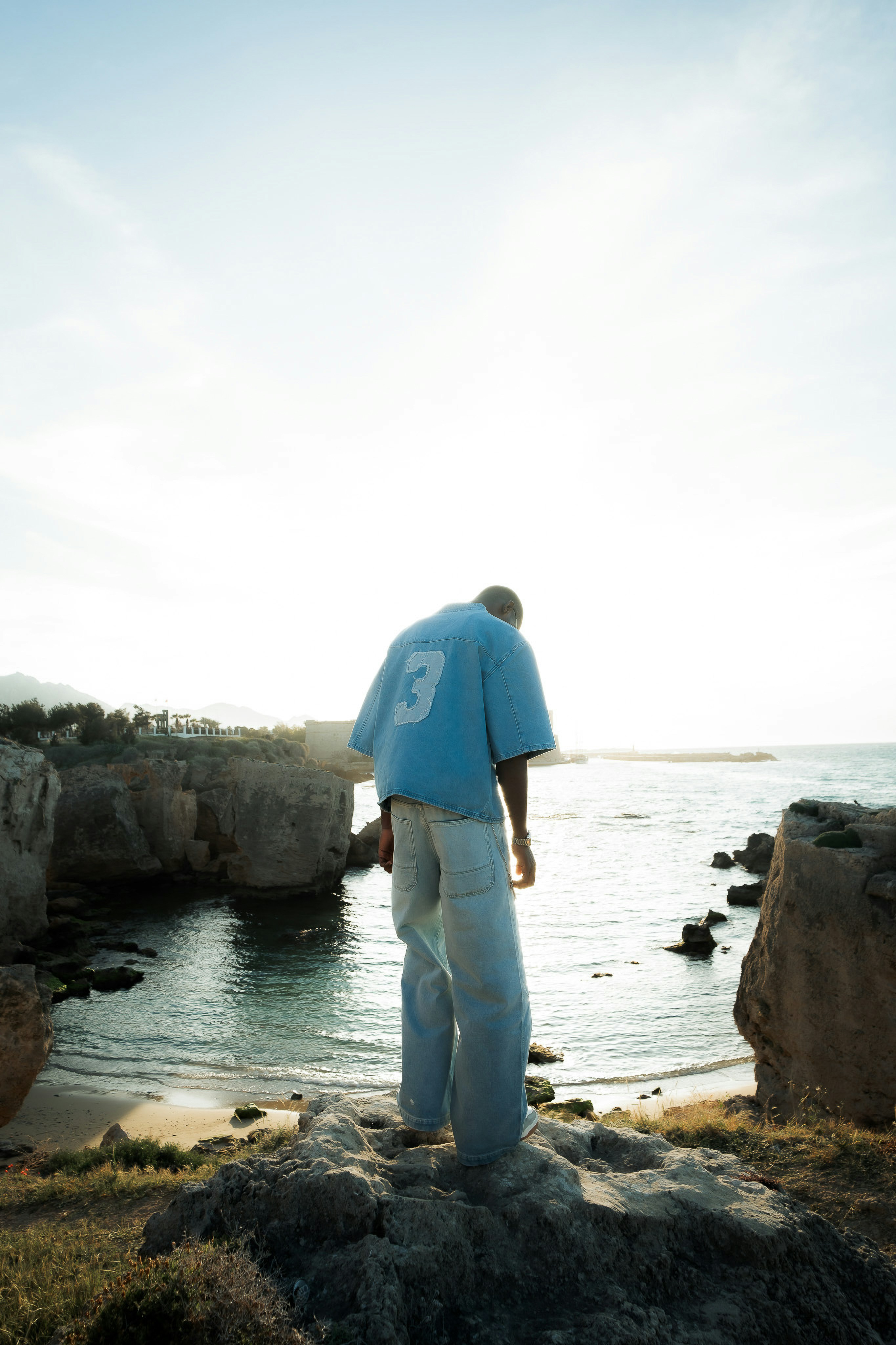 A person in a denim shirt with a number three on the back standing on a rocky cliff