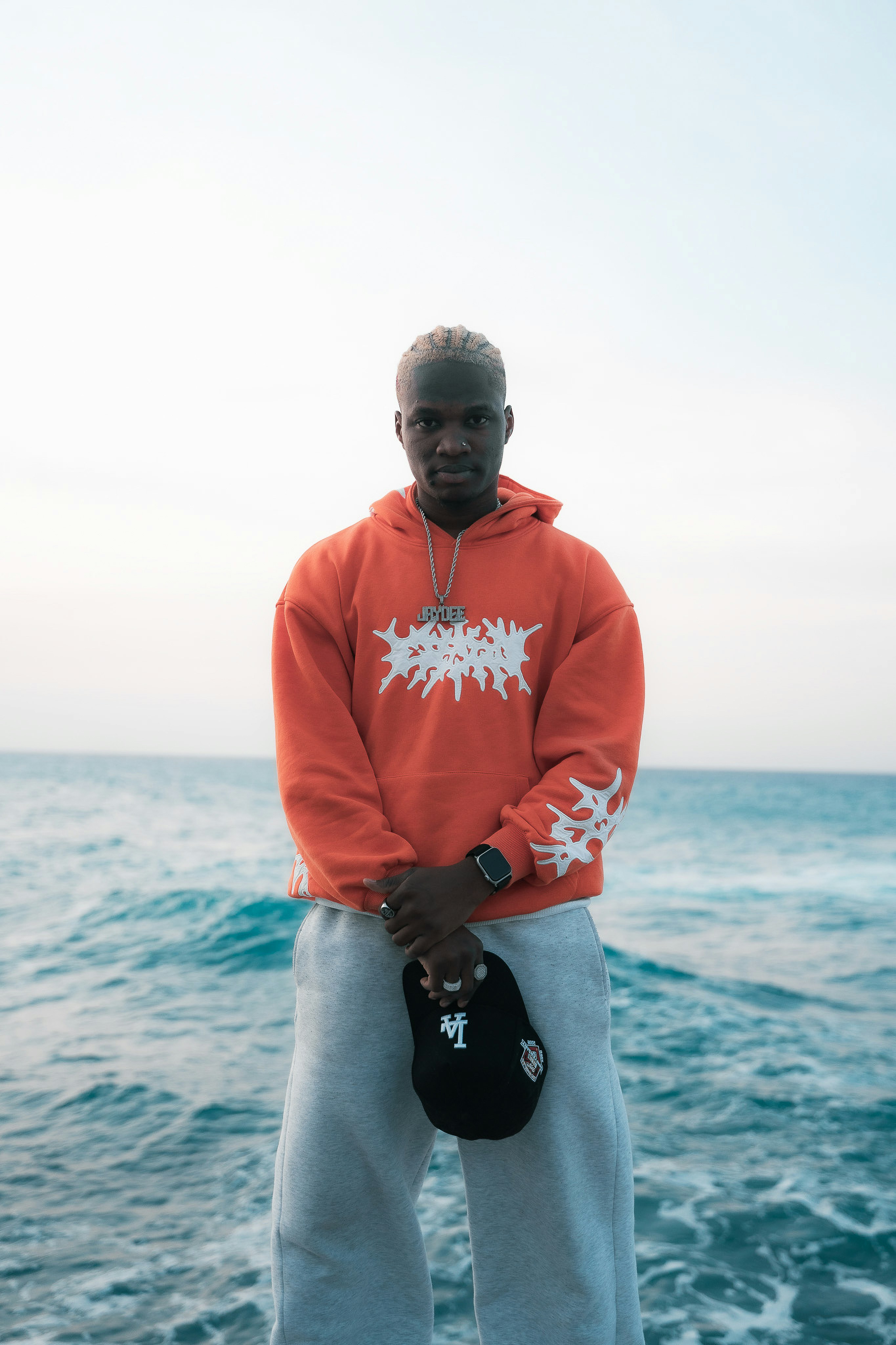 A man in an orange hoodie and grey sweatpants standing before the ocean - 相关推荐