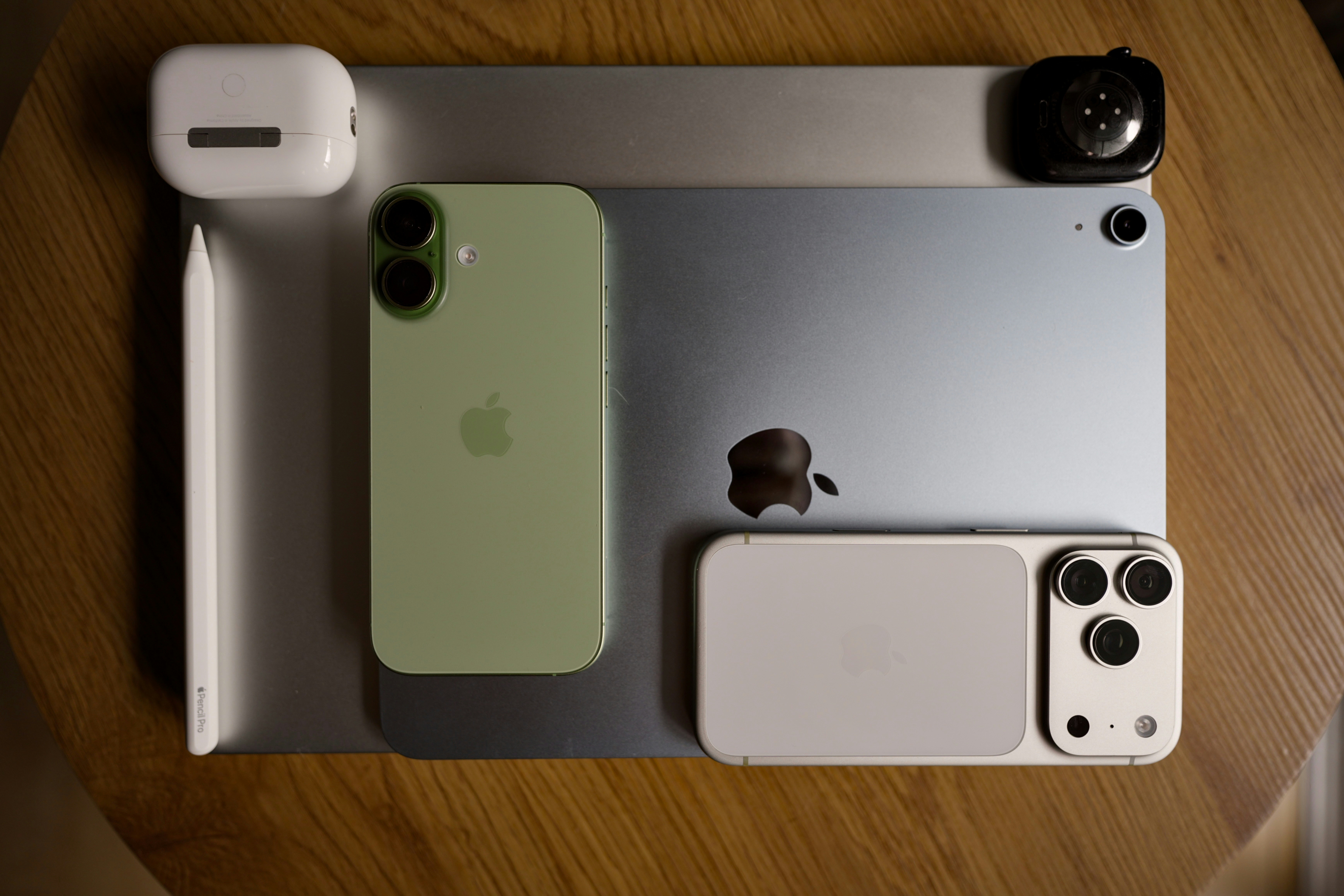 A green smartphone, a white smartphone, a tablet, and accessories on a wooden table