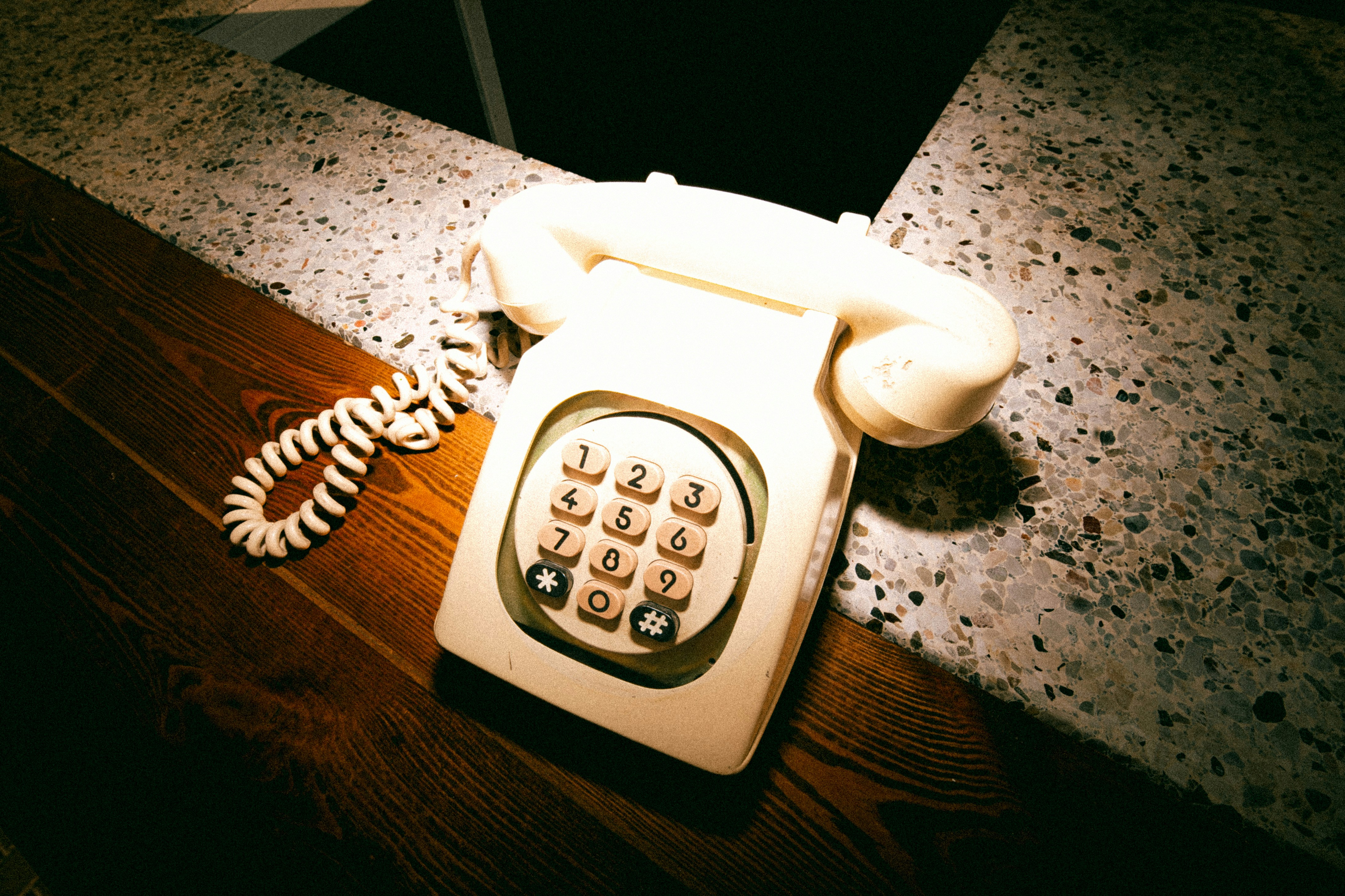 A vintage cream push-button telephone on a wooden surface beside a speckled stone counter