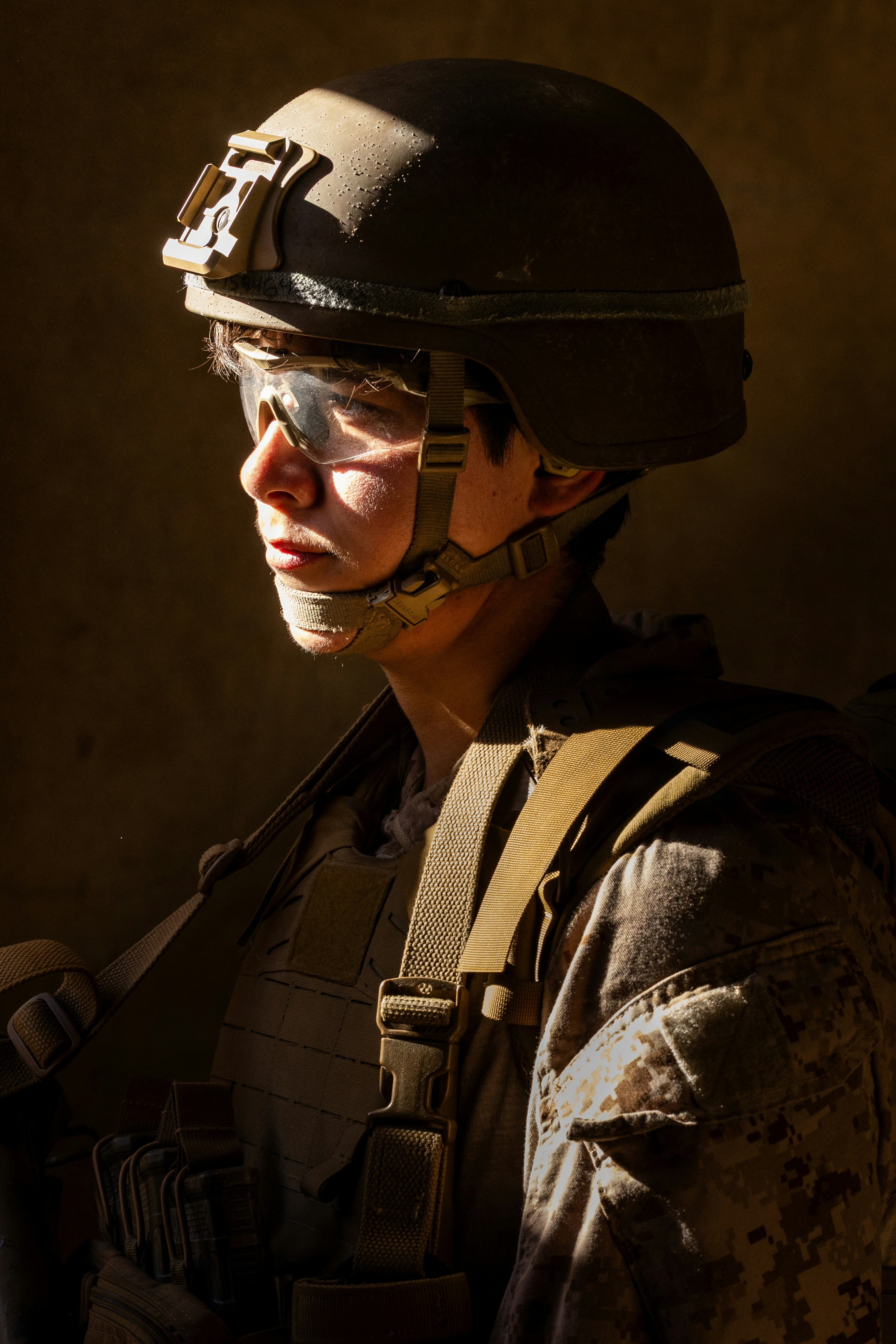 A person in a military helmet and tactical vest illuminated by warm light