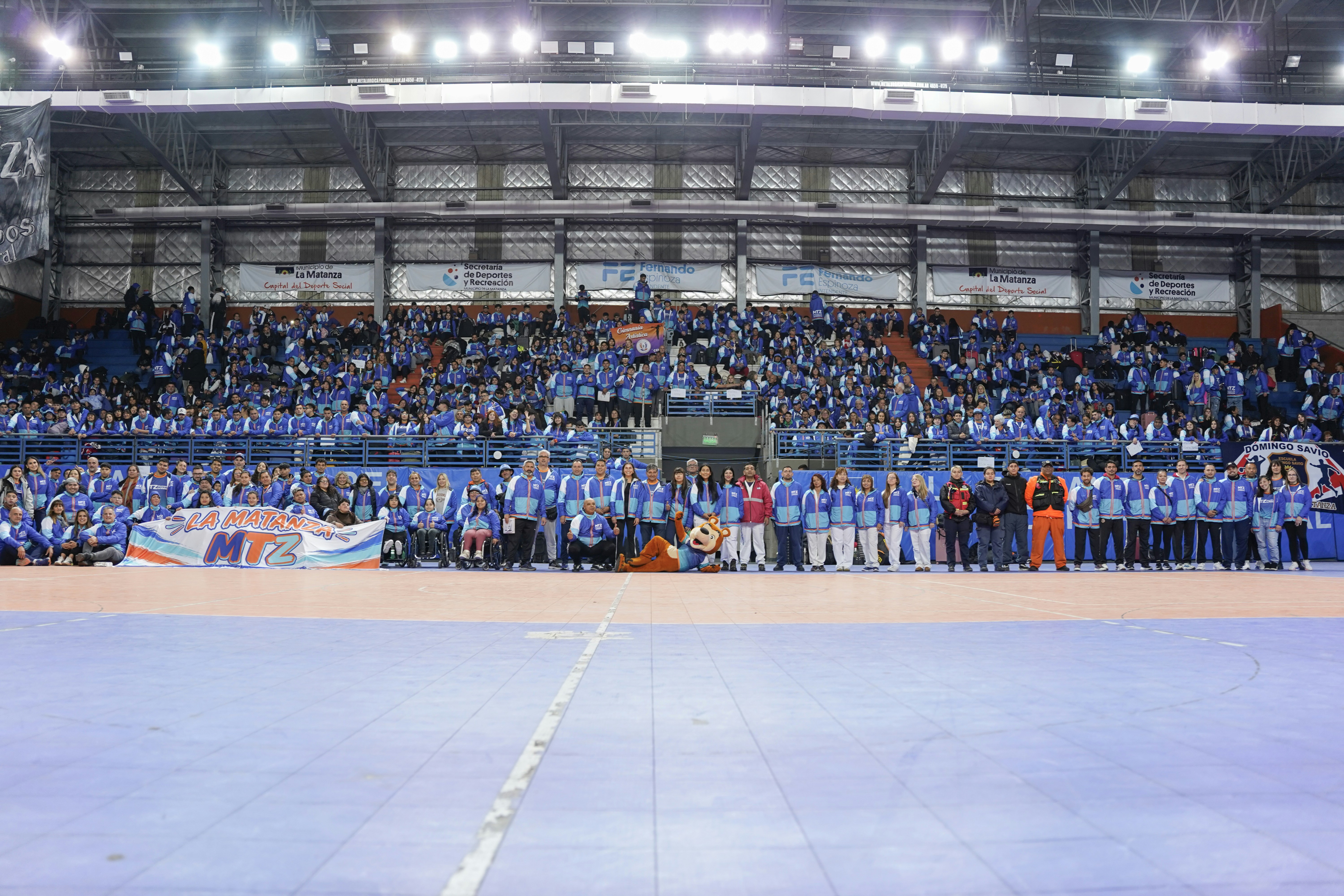 A large group of people in blue and white jackets posing in a sports arena