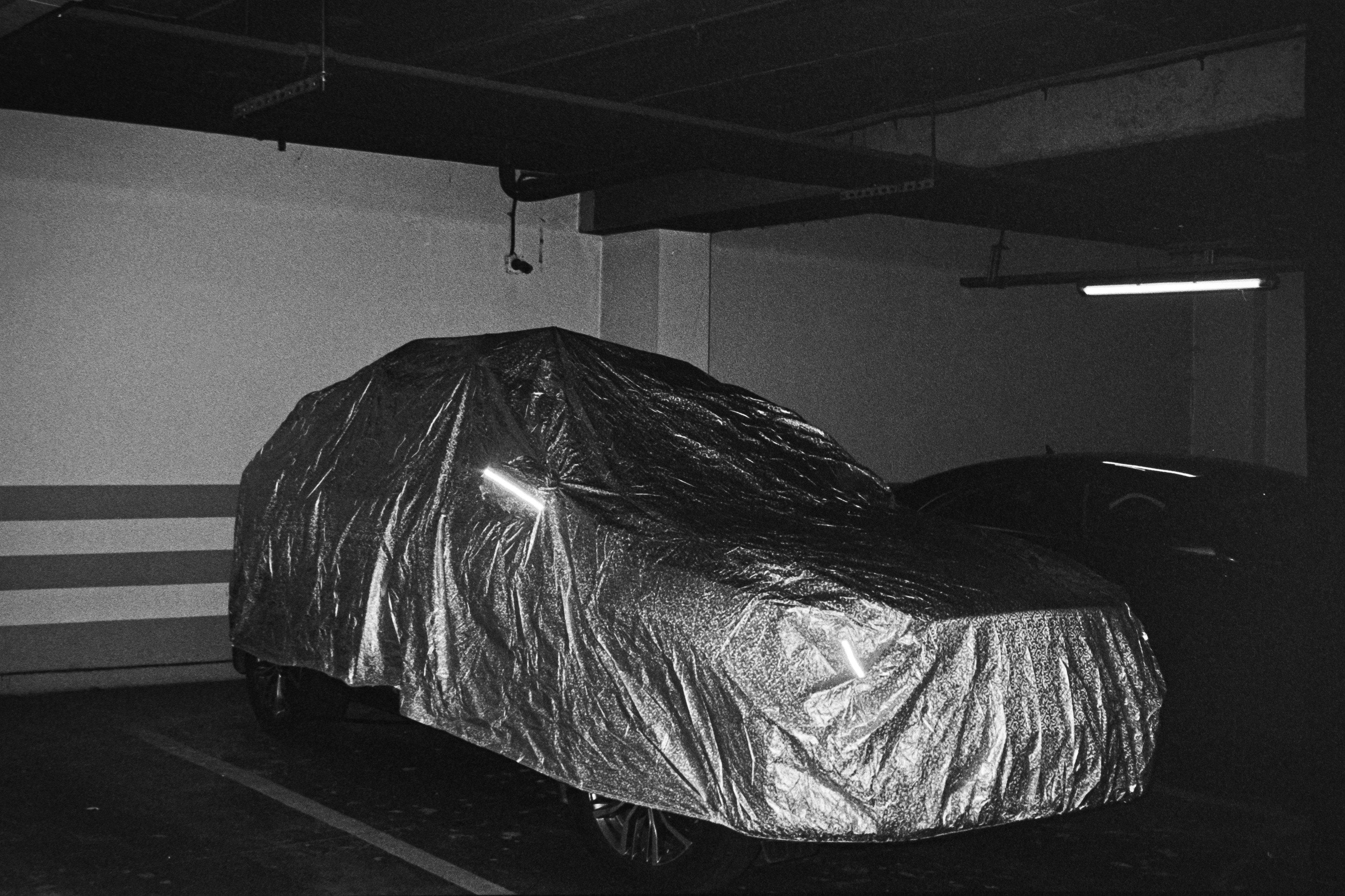 A car covered in a reflective silver tarp parked in a dim concrete parking garage - 相关推荐