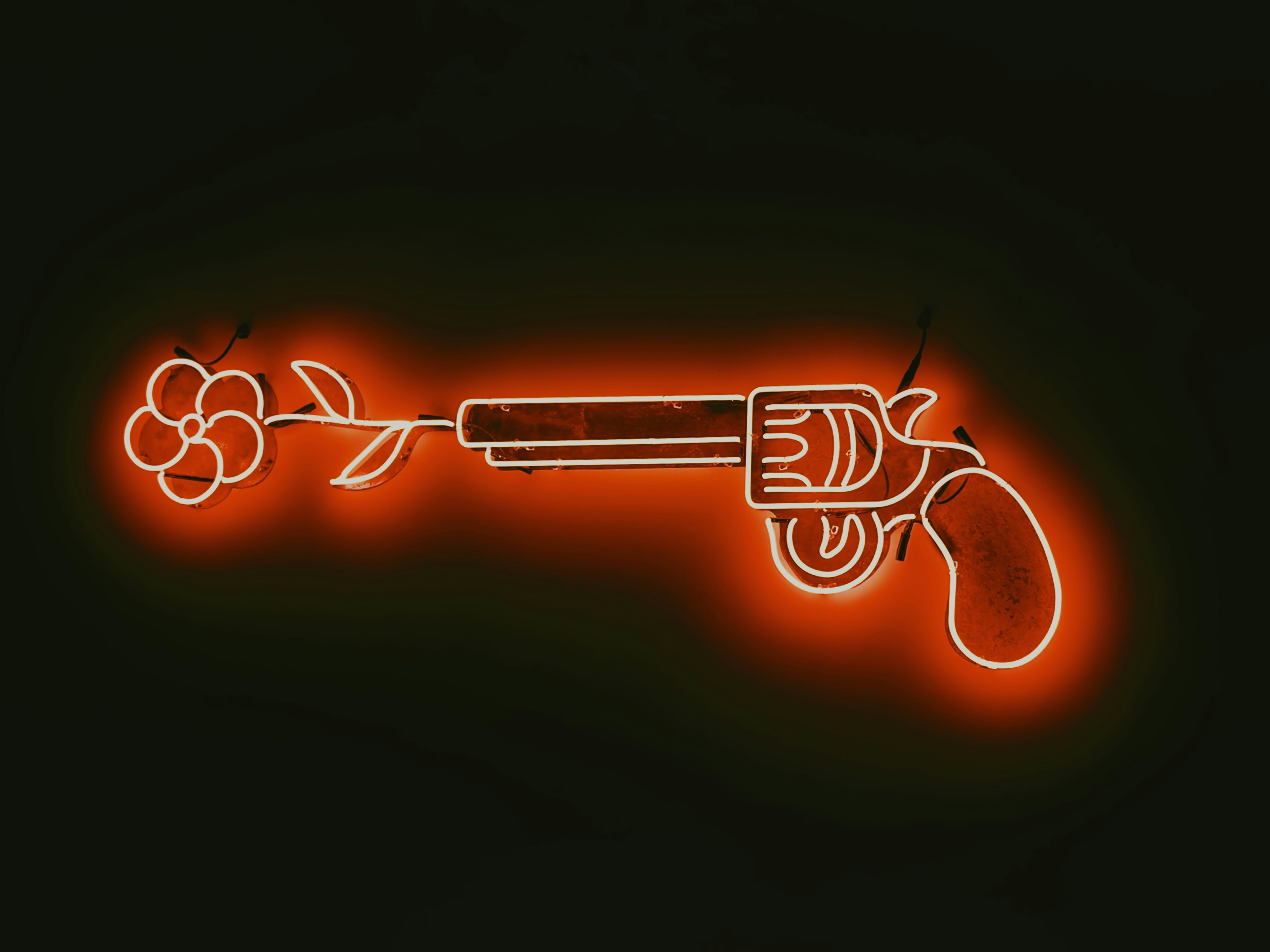A bright red neon sign depicting a revolver with a flower emerging from the barrel