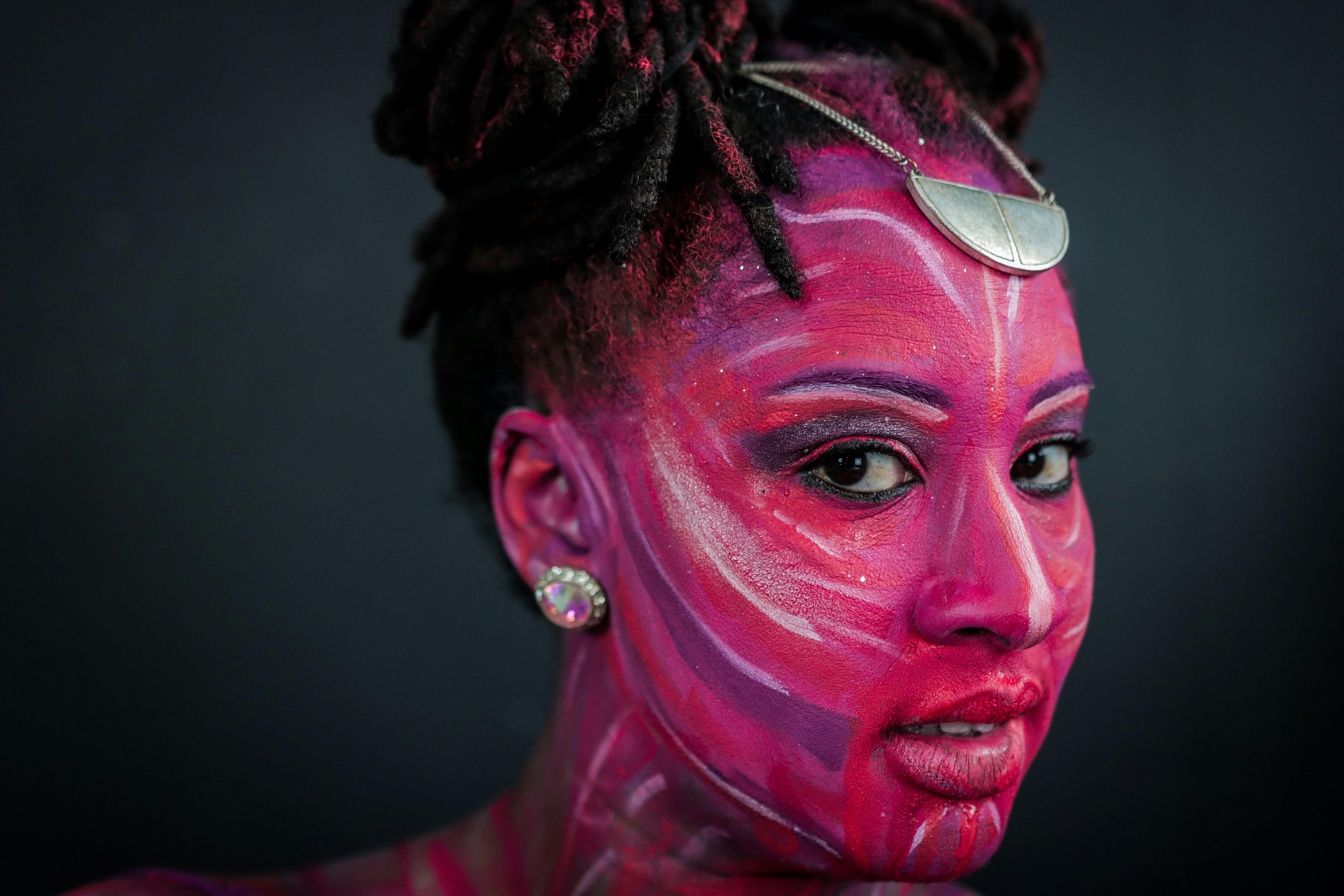 A person with vibrant pink and purple face paint and dark hair in buns