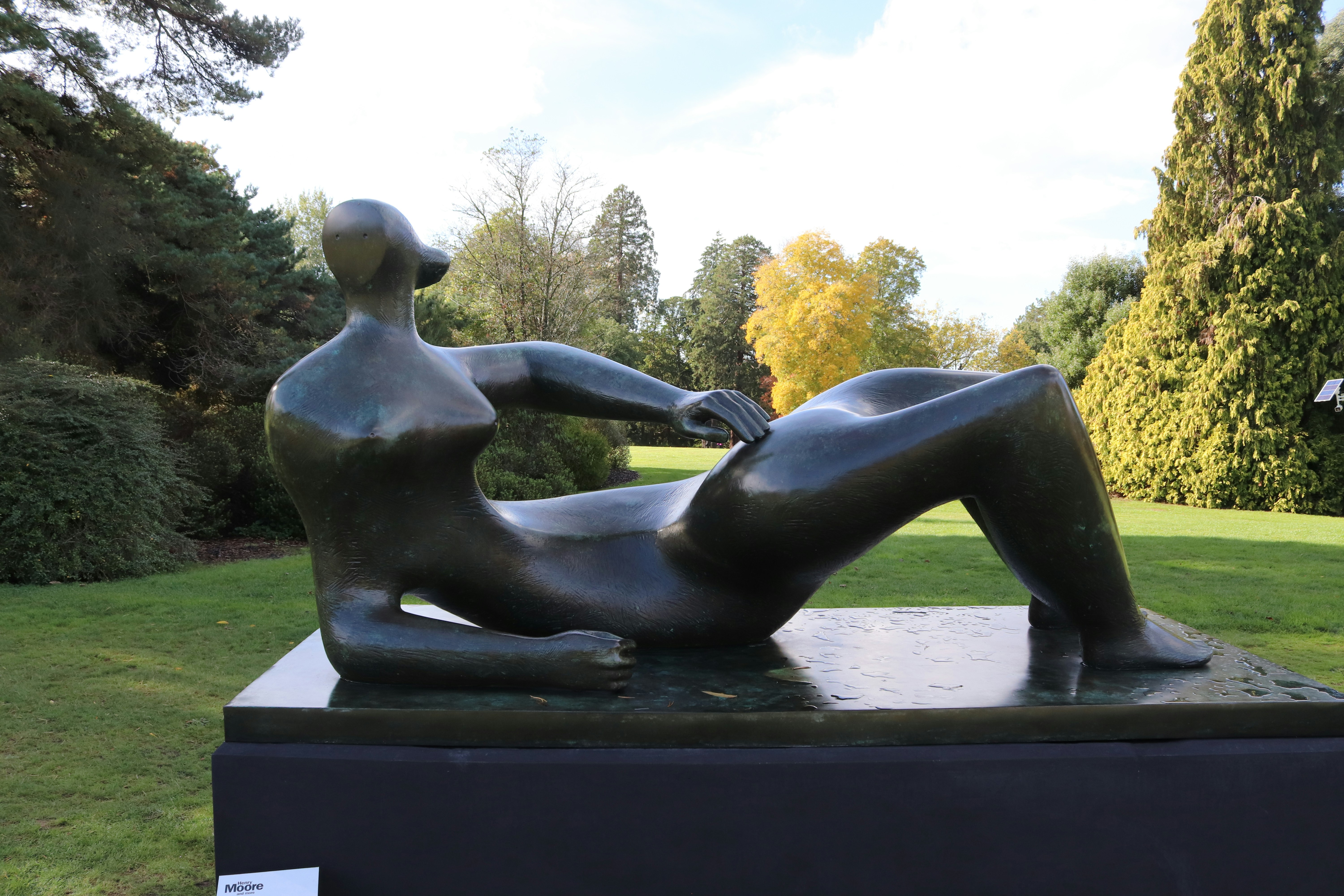 A bronze reclining figure sculpture by Henry Moore in a park with autumn trees