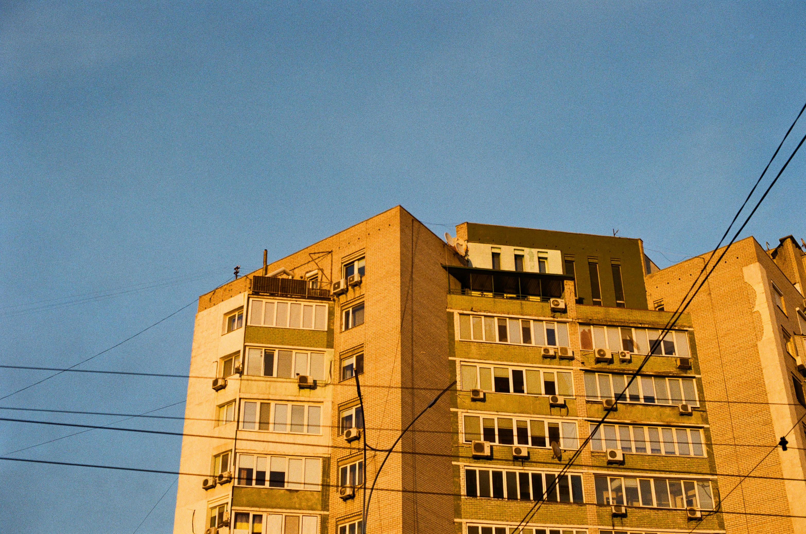 A tall brick apartment building with many balconies under a clear blue sky